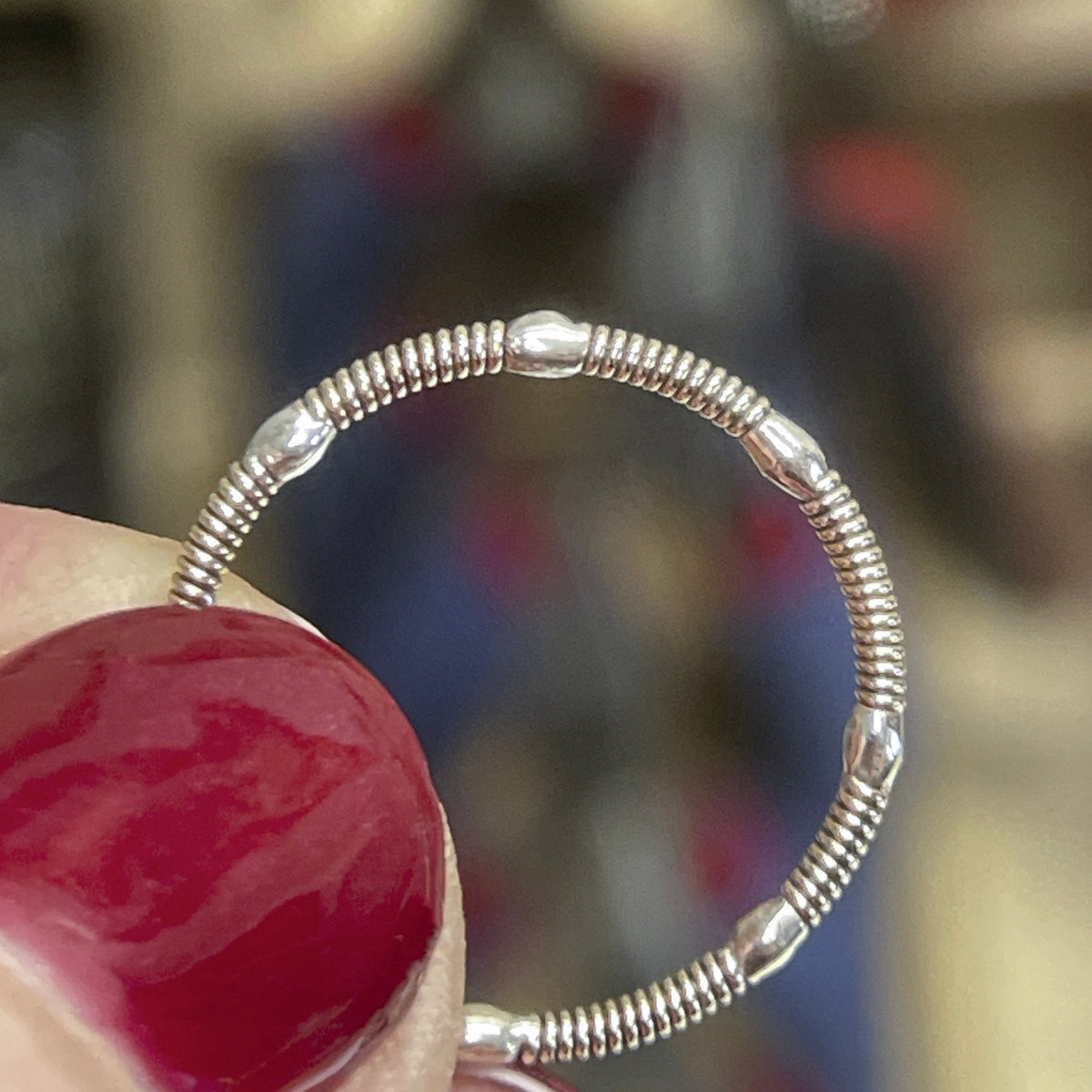 Silver guitar string ring held by a hand with a blurred background