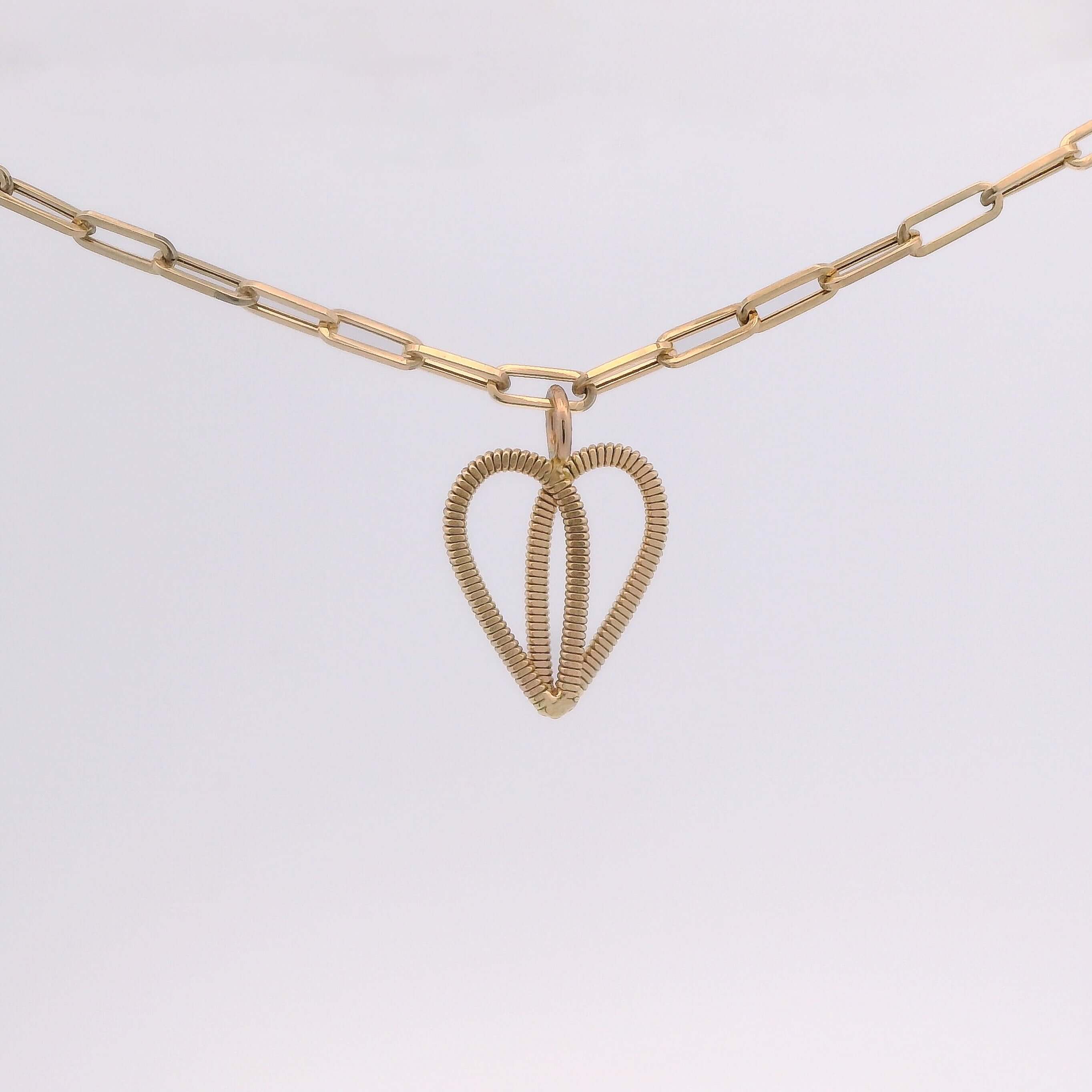 Gold guitar string heart on gold paperclip chain with light background.