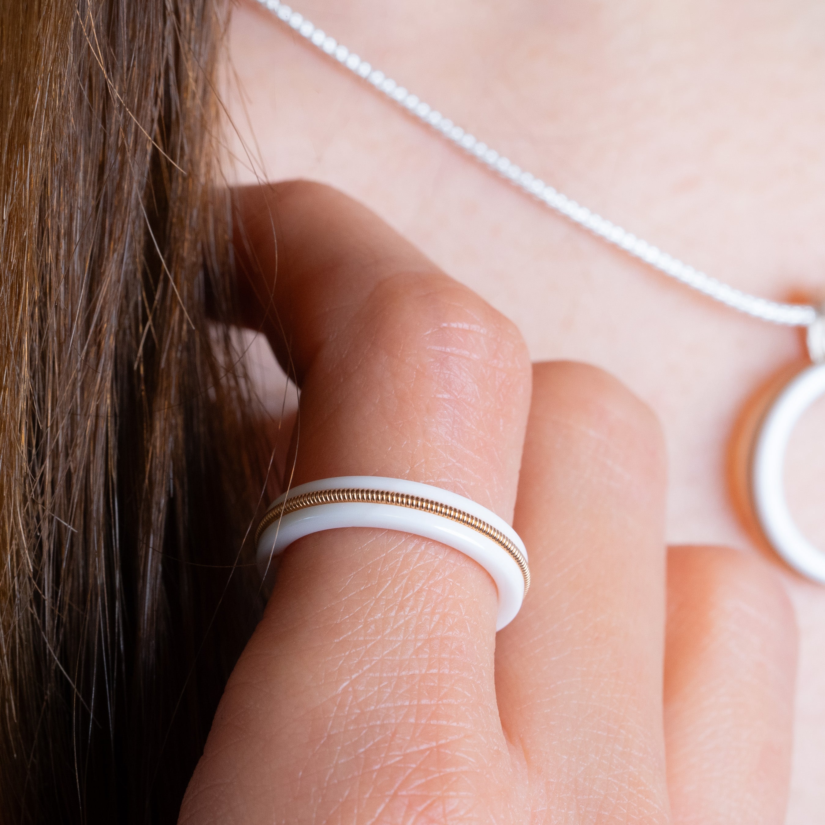 Close up of white ring with inlaid guitar string on model.