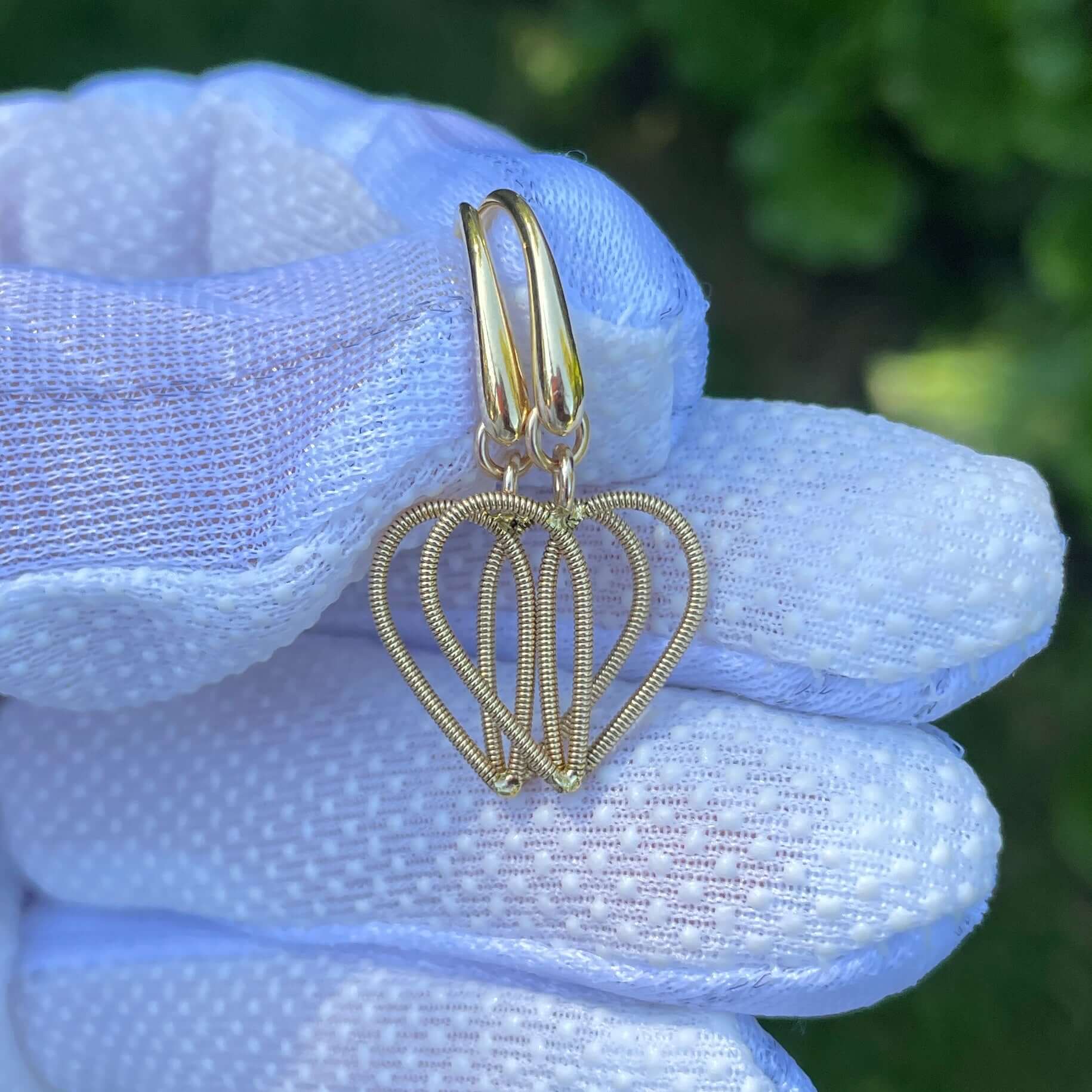 Golden guitar string heart earrings held in a white gloved hand