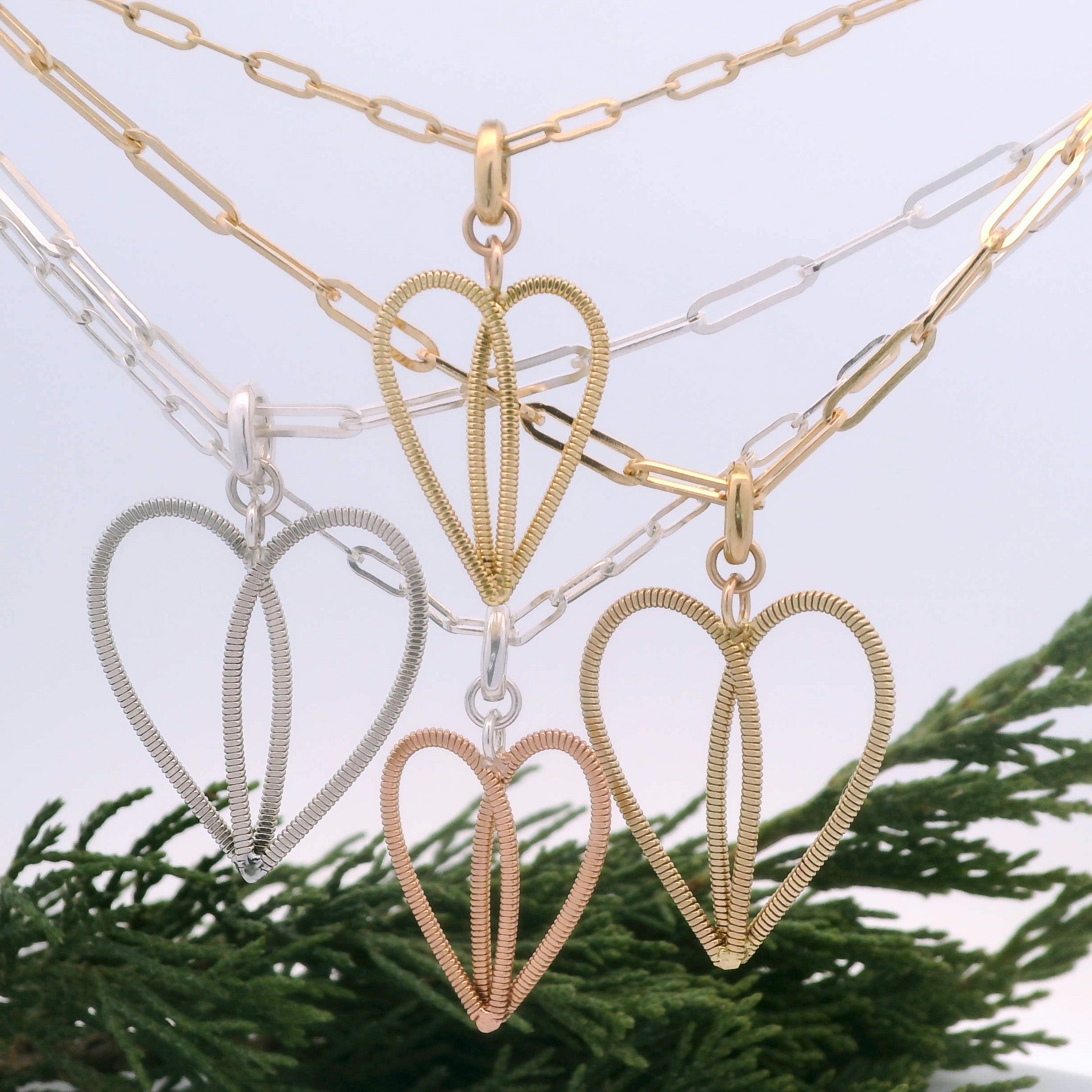 4 heart necklaces on paperclip chains with pine bow in the background