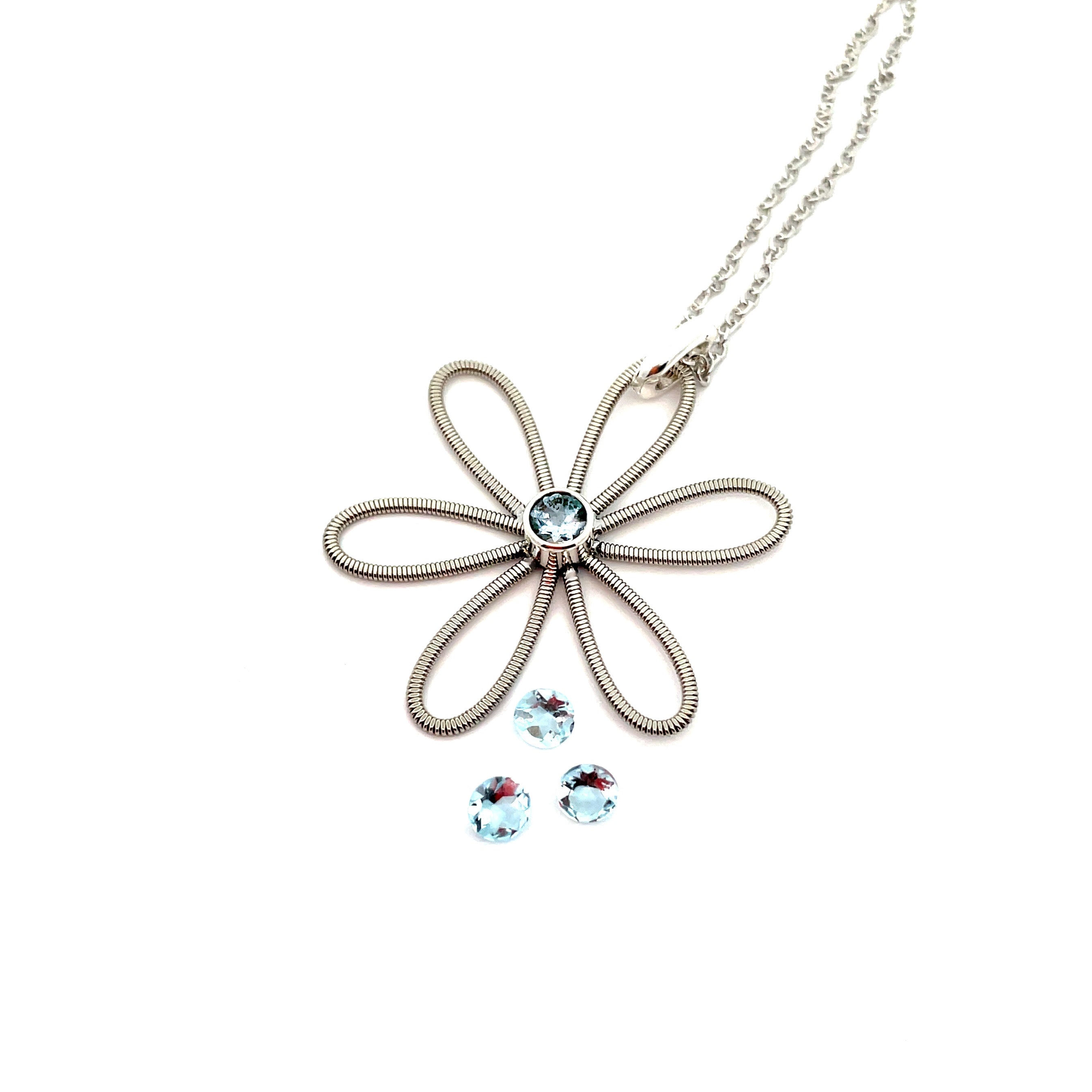 Electric guitar string flower with aquamarine at it's centre laying on white background with 3 loose aquamarine gemstones.