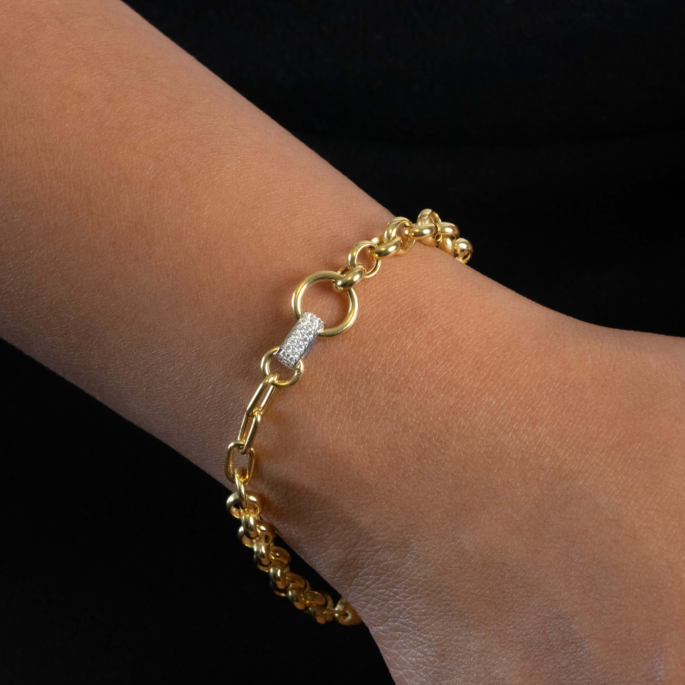Gold bracelet with a diamond clasp on a wrist against a black background