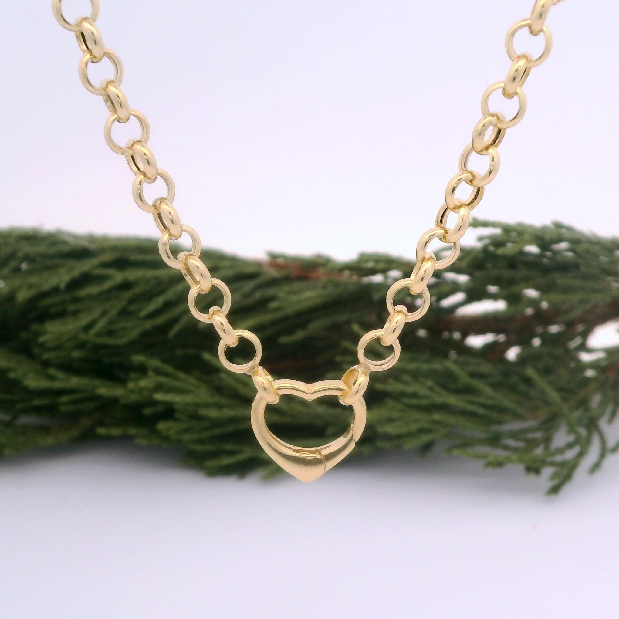 Gold chain necklace with a heart-shaped pendant on a white background with greenery.
