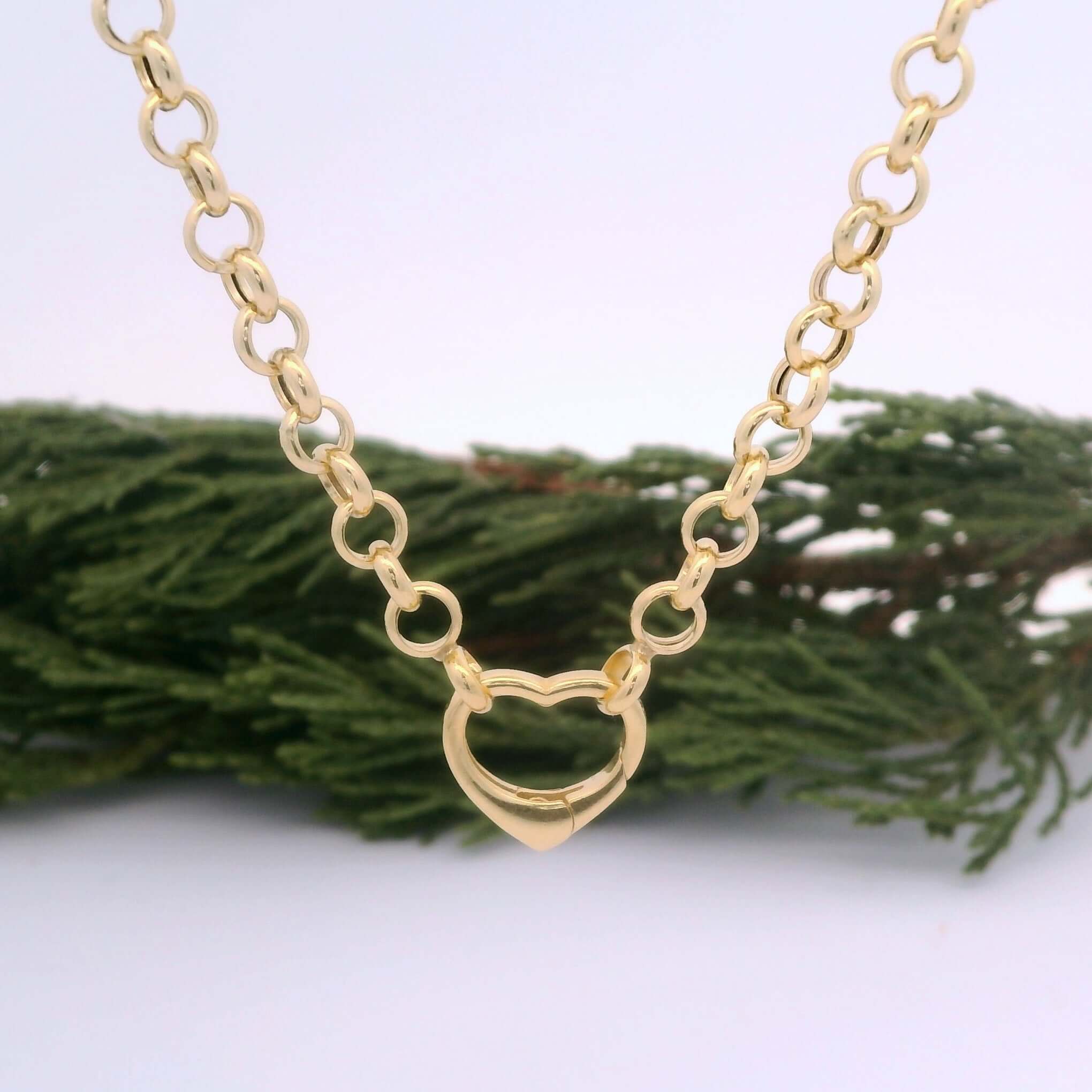 Gold chain necklace with a heart-shaped pendant on a white background with greenery.