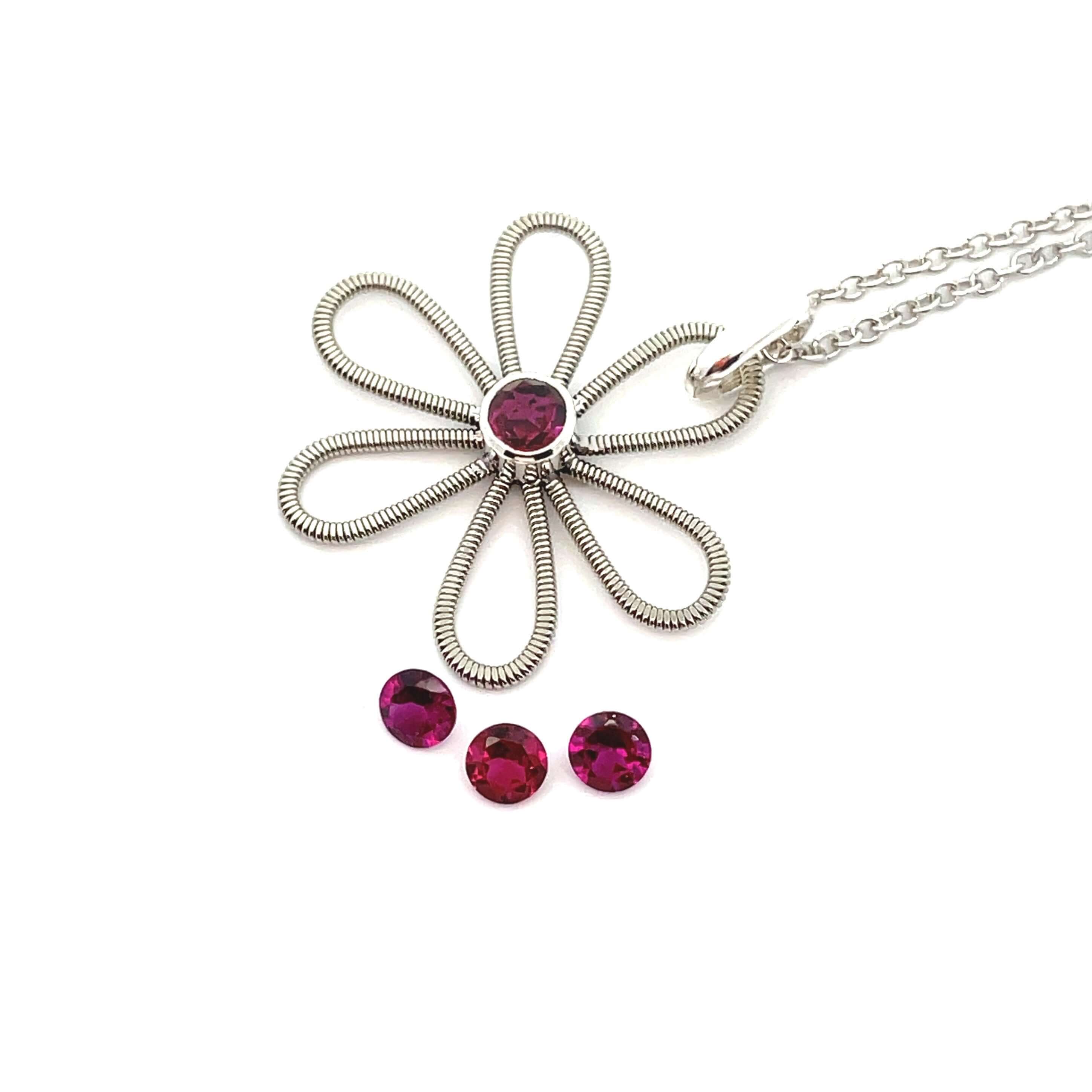 Electric guitar string flower pendant with garnet gemstone in the centre on a white background with three loose garnets.