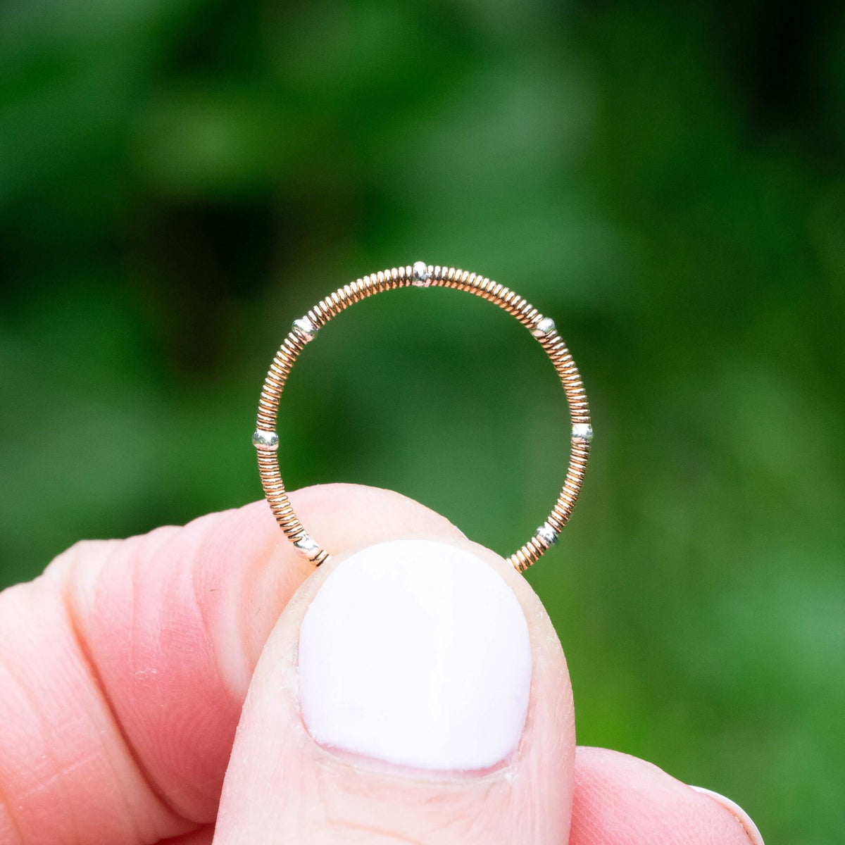 Rose guitar string ring with silver accents held in fingers with a green background