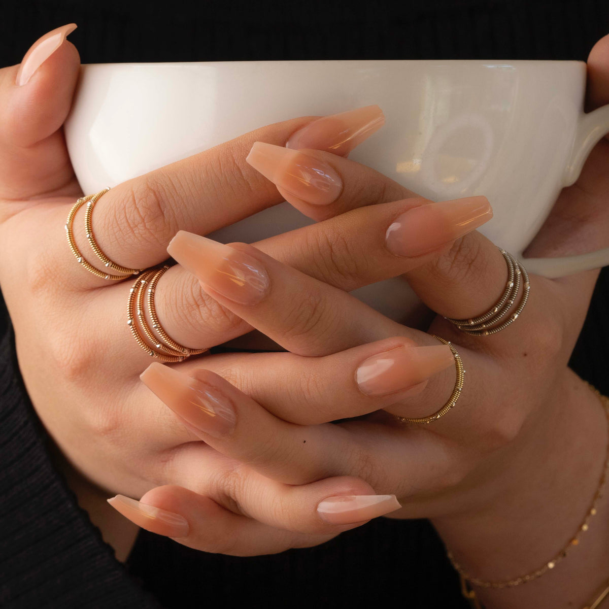Close-up of hands with gold rings holding a white mug.