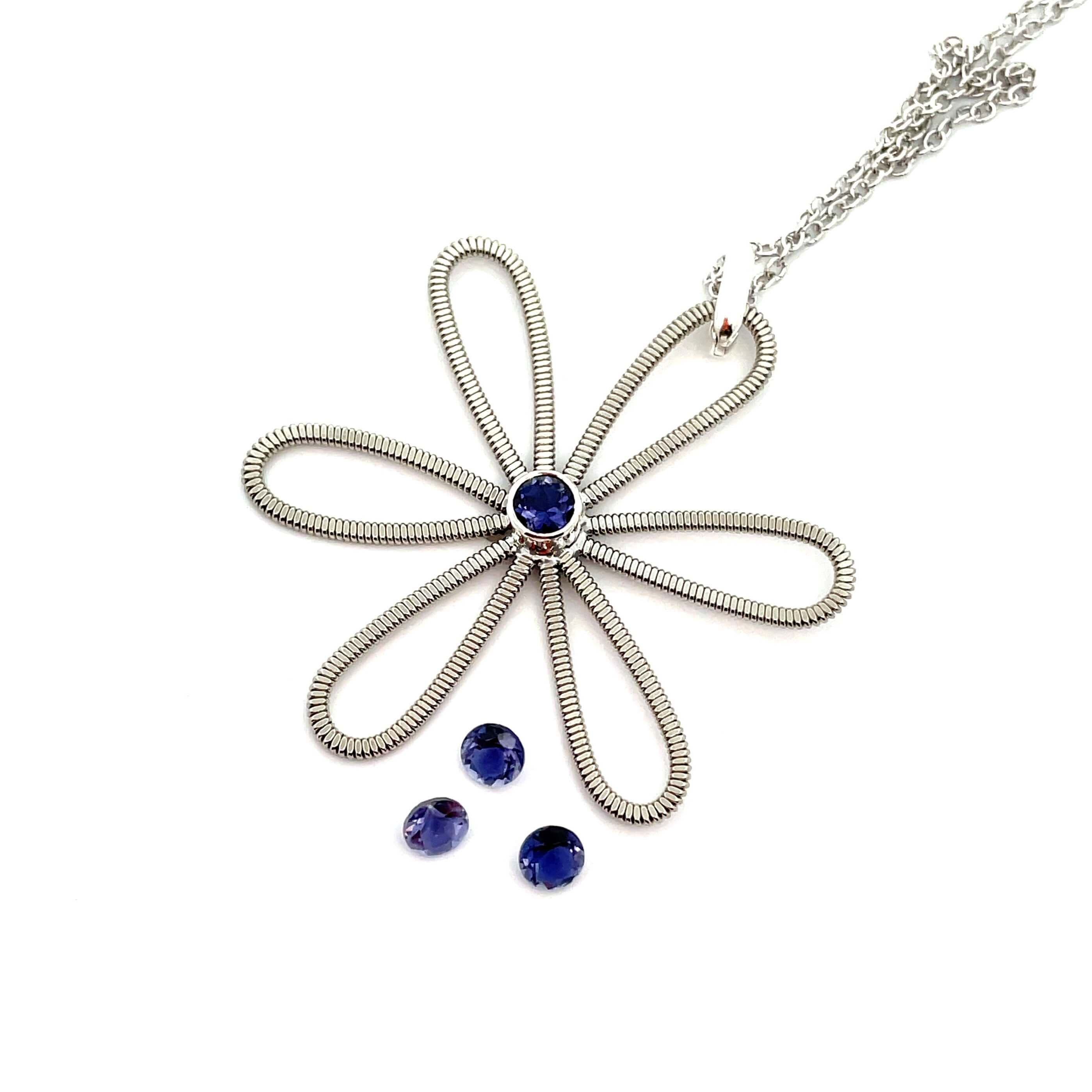 Electric guitar string flower with an iolite gemstone at it's centre laying on white background.