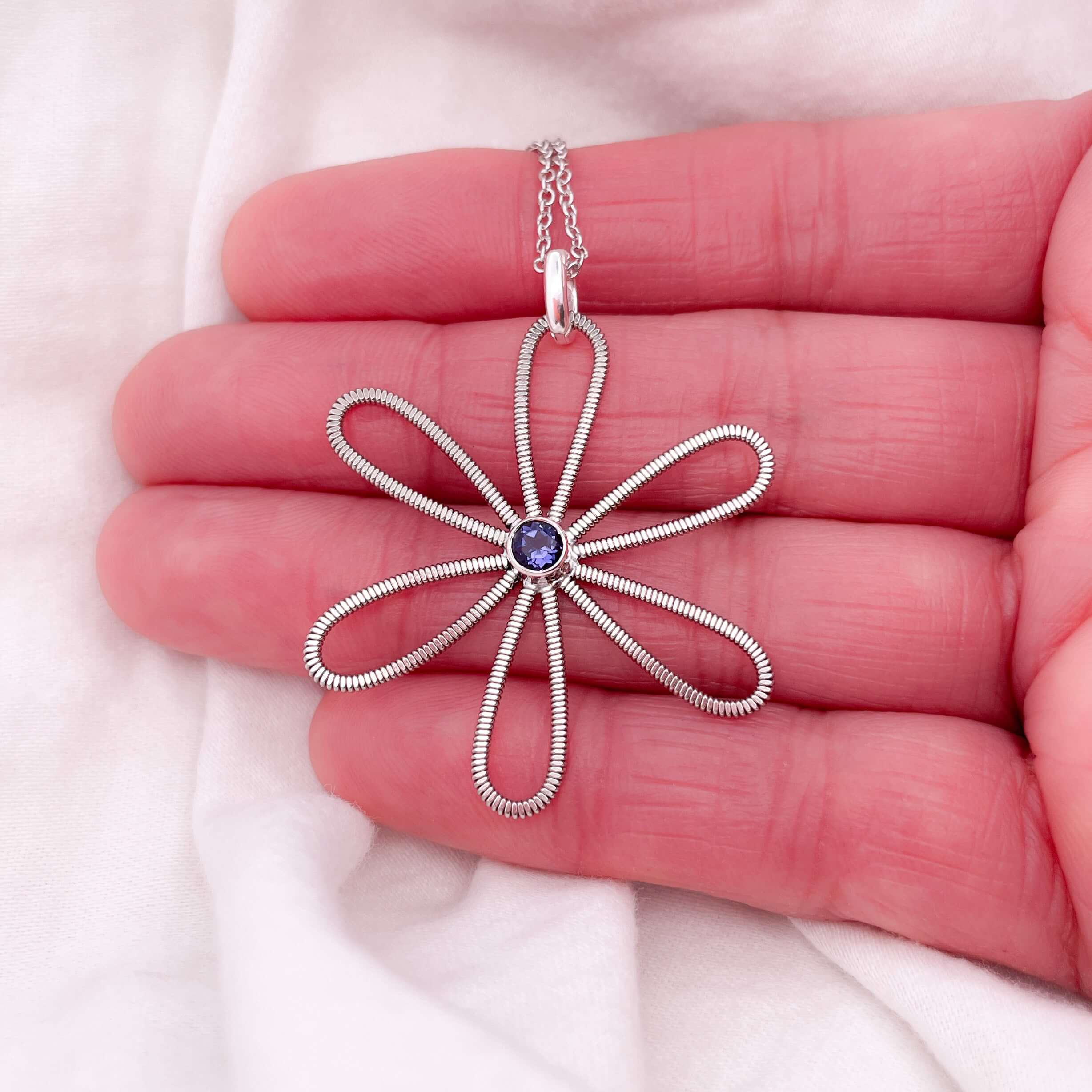 Electric guitar string flower with an iolite gemstone at it's centre on a white background.