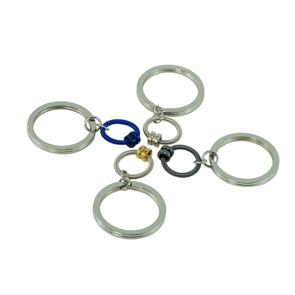 four bass guitar string keychains in silver, blue, and grey on a white background