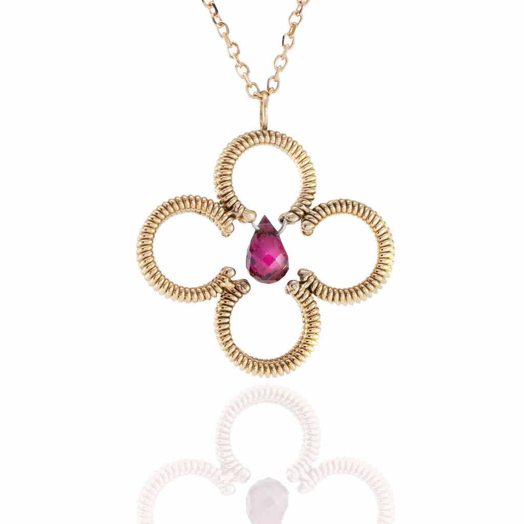 acoustic guitar string clover shaped pendant with a central red tourmaline gemstone with a rose gold chain on white background with reflection