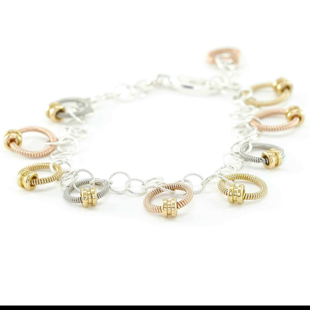 bracelet made of small rings of tri-metallic guitar string and ball ends laid out on a white background