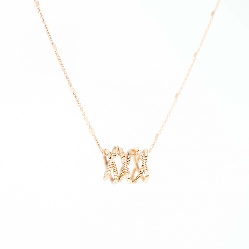 guitar string helix shaped necklace with 18k rose gold chain on a white background