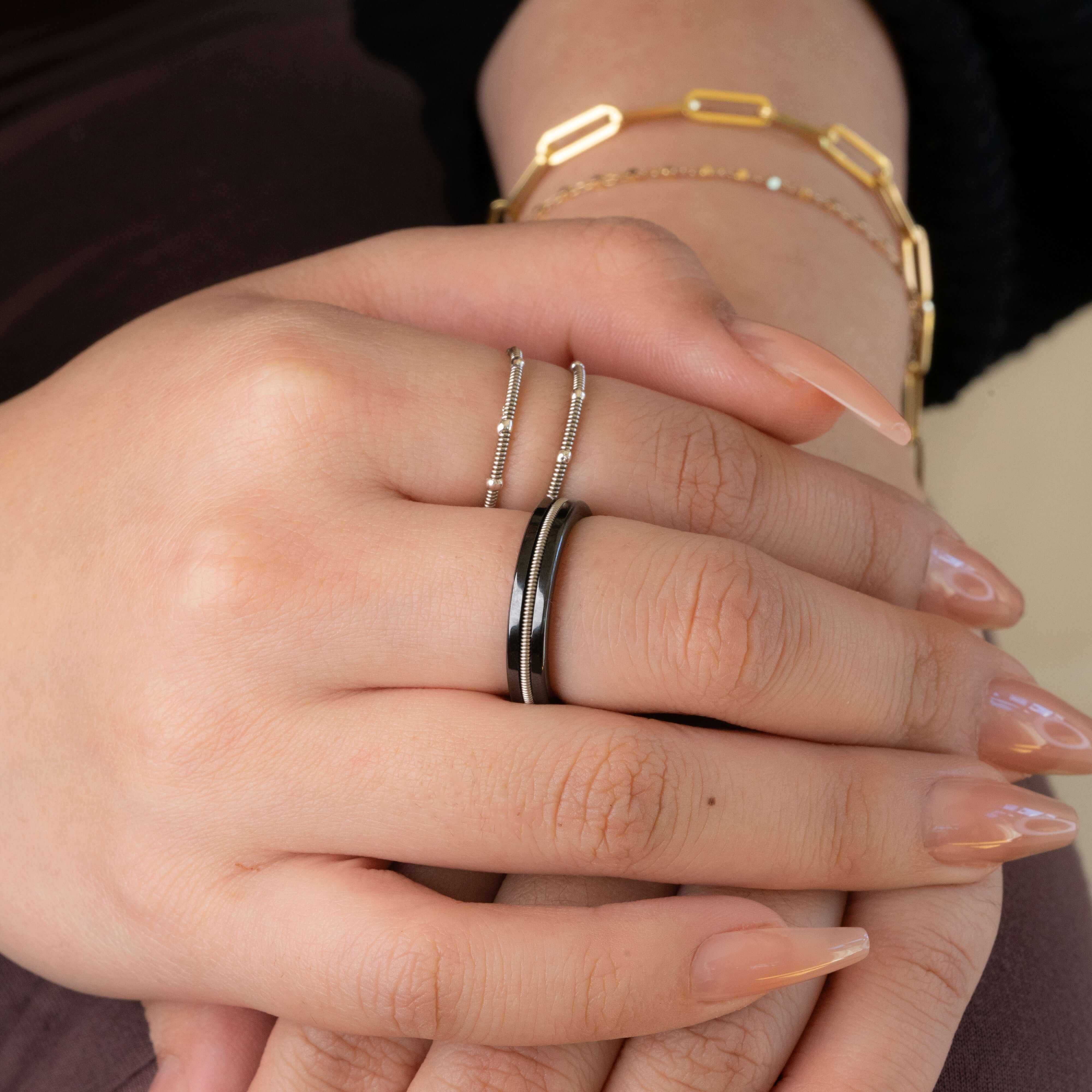 black guitar string ring and two silver guitar string rings on woman's hands crossed on lap