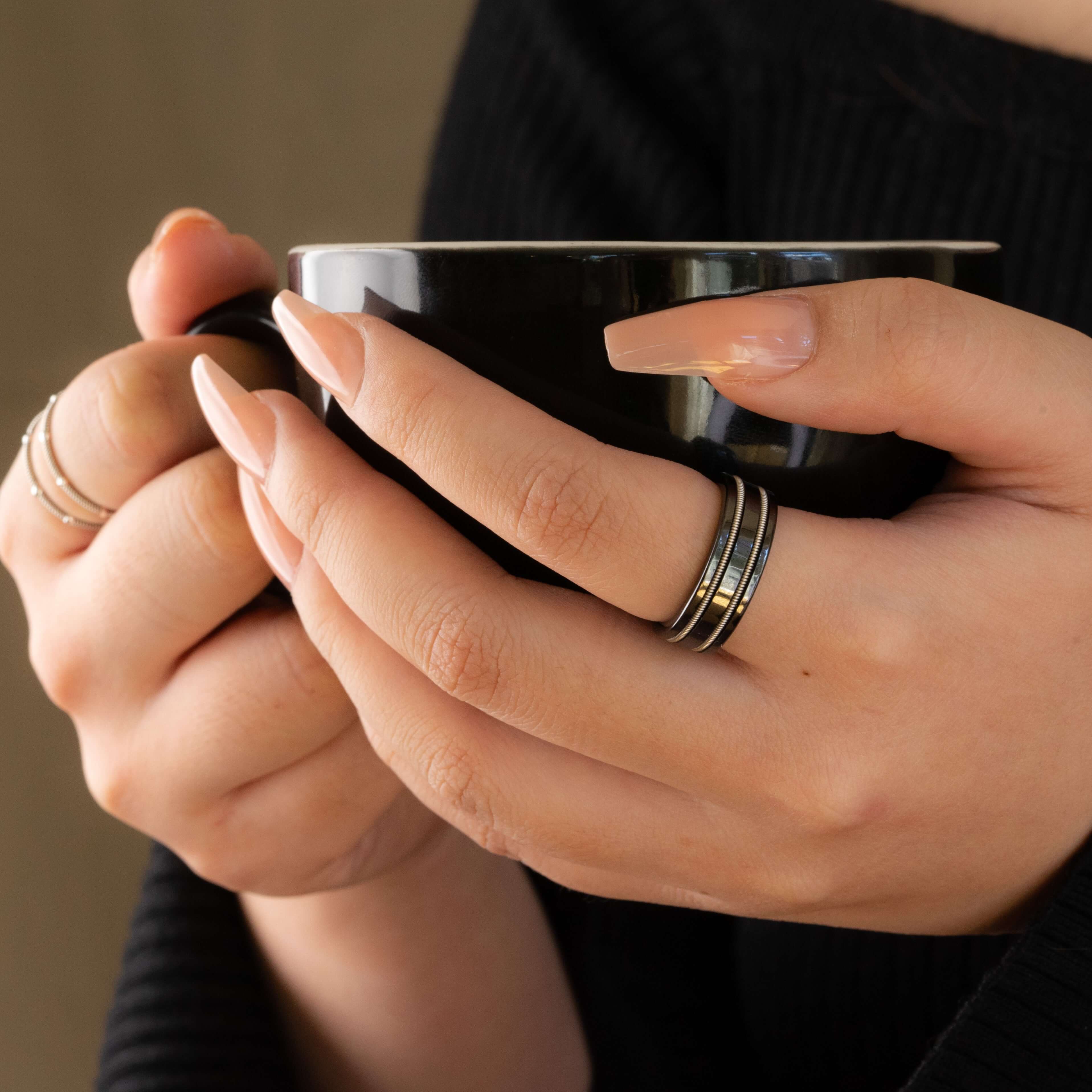 black guitar string ring on woman's hand holding black coffee cup.