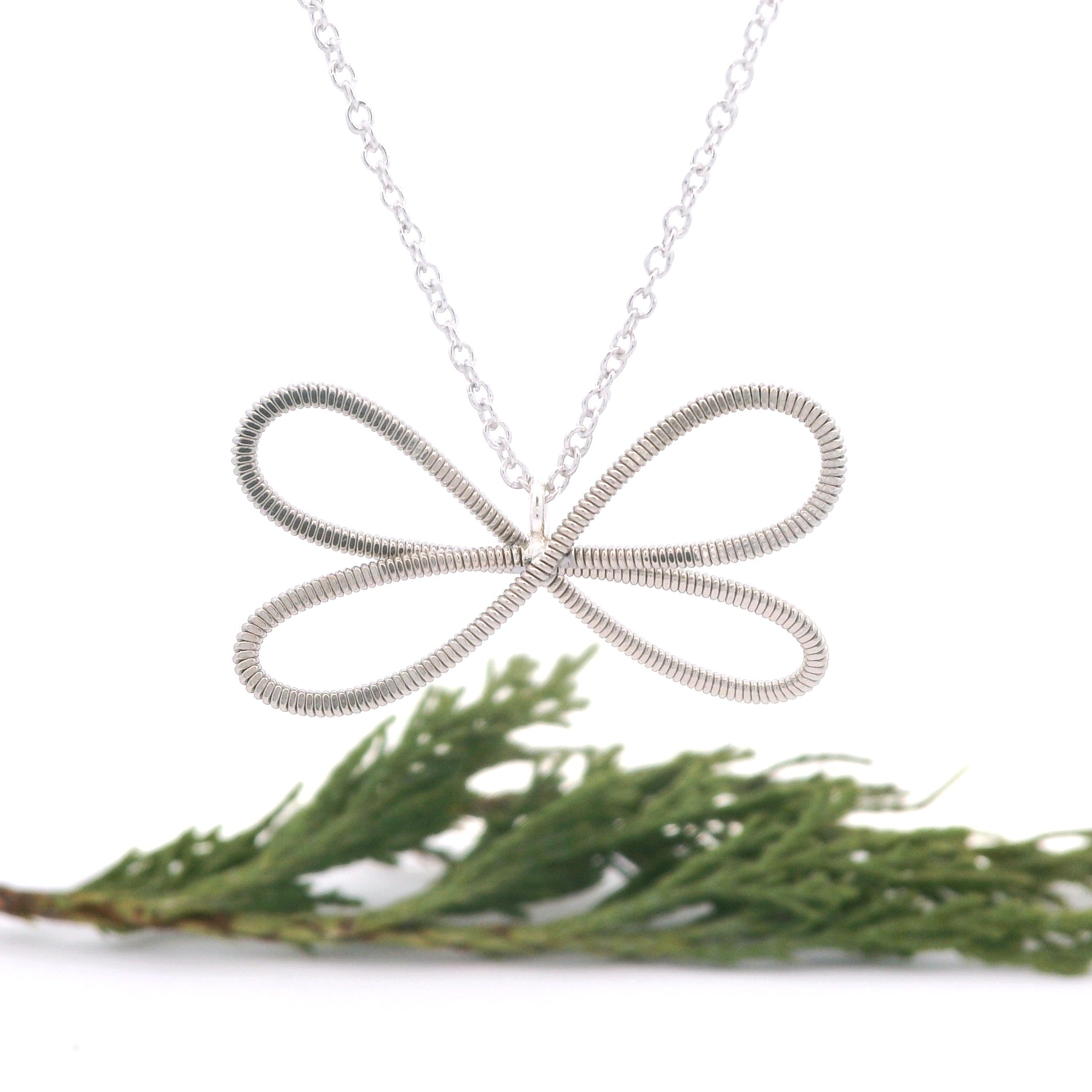 Electric guitar string dragonfly necklace on a white background with greenery