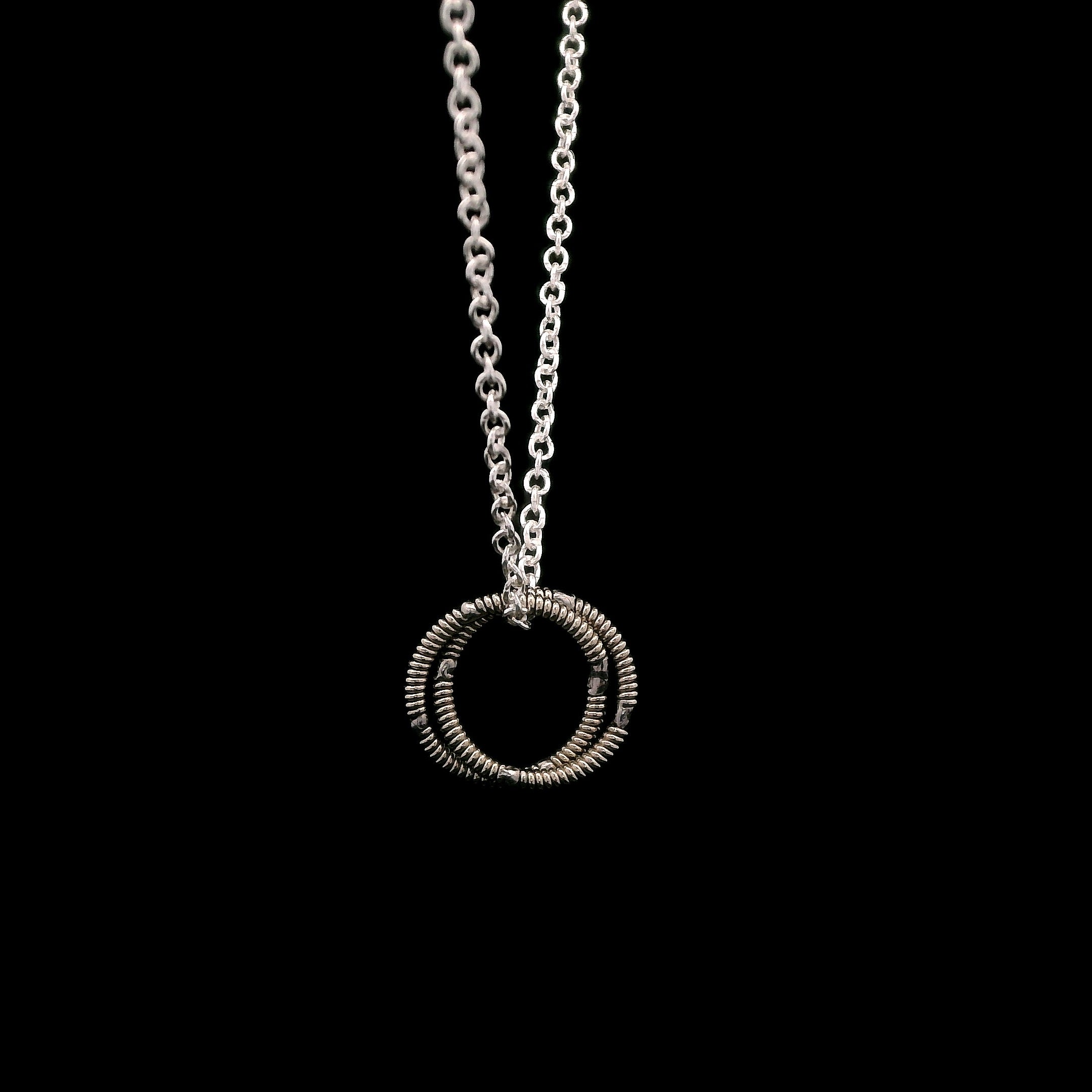 Silver necklace with a circular pendant on a black background