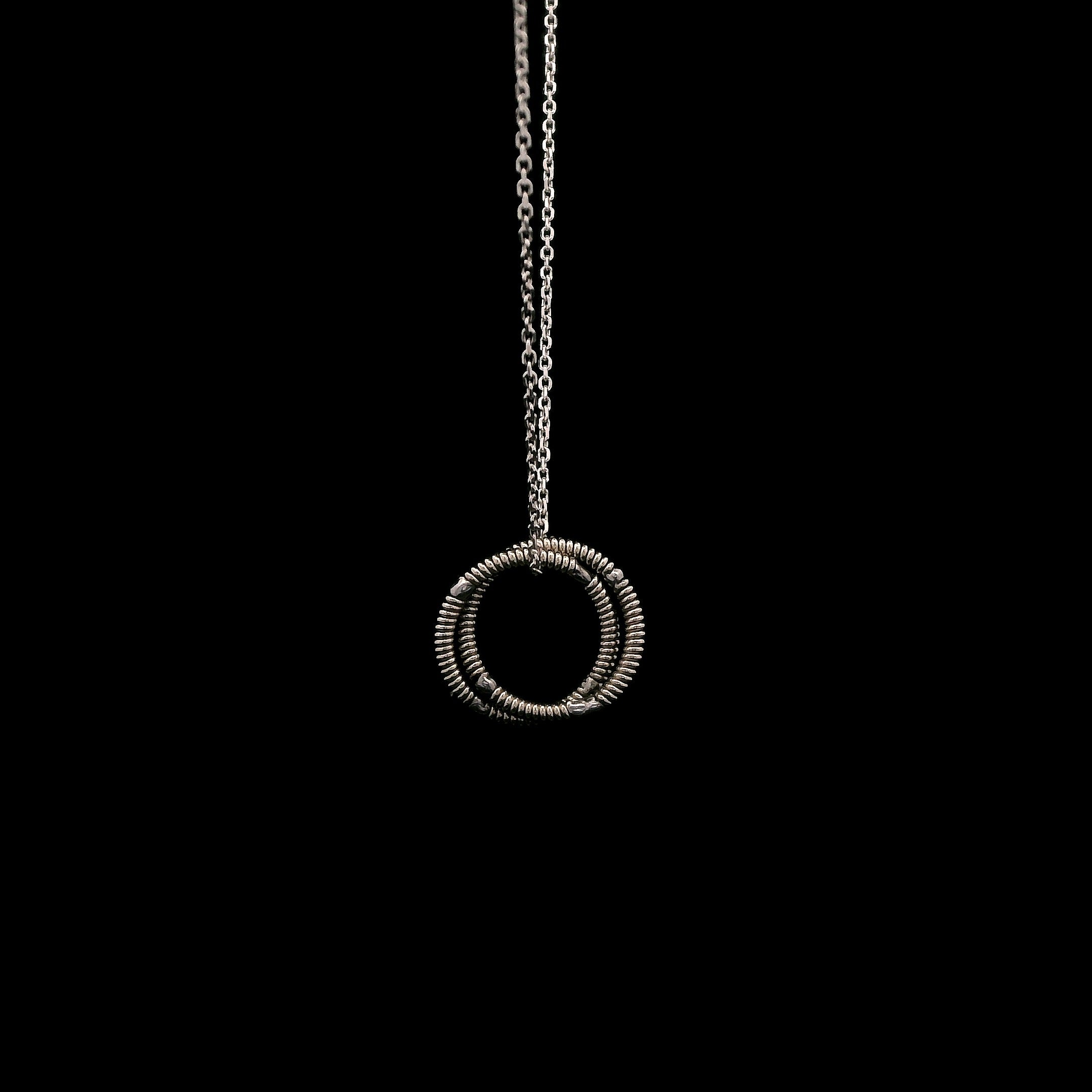 Silver necklace with a circular guitar string pendant on a black background