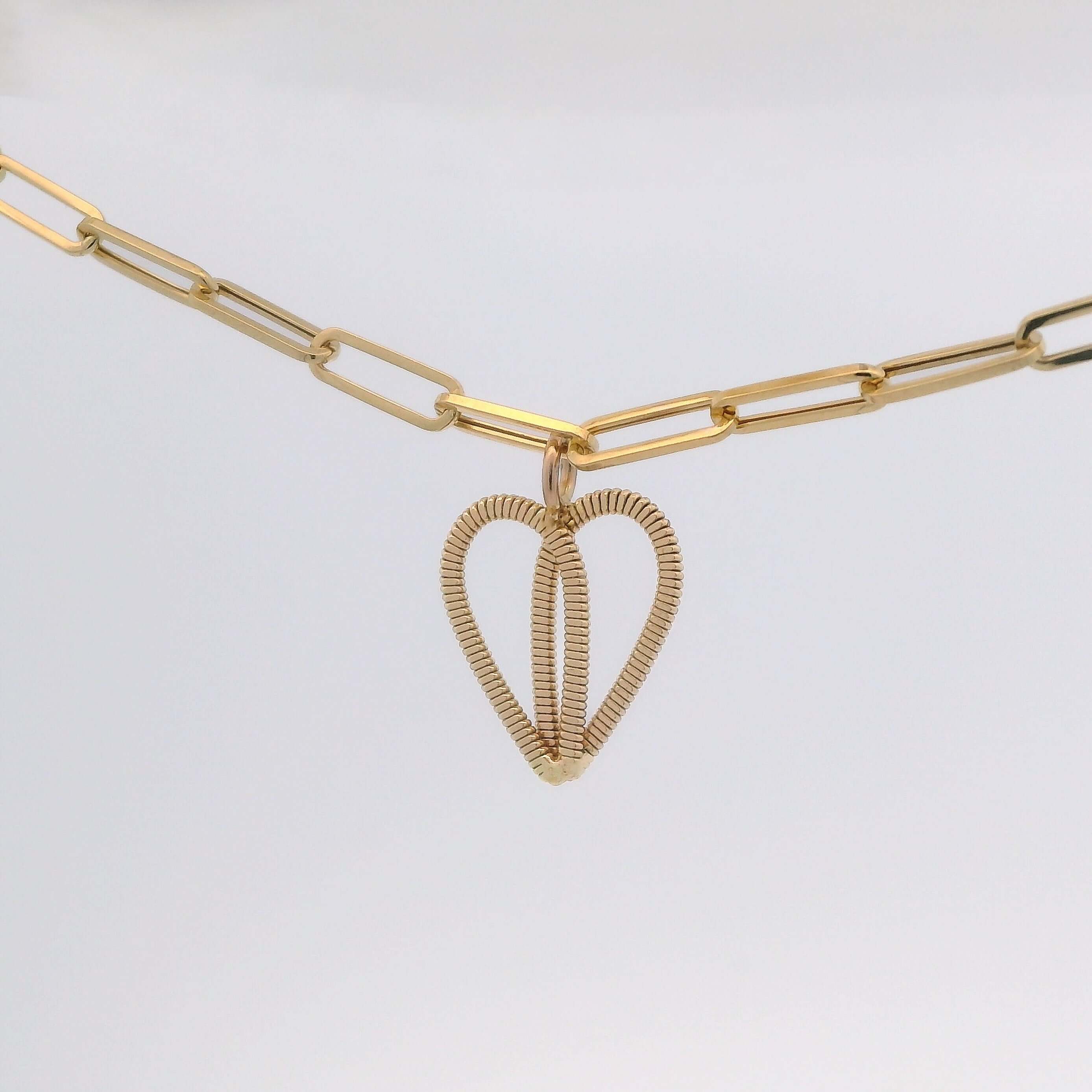 Gold guitar string heart on gold paperclip chain with light background.