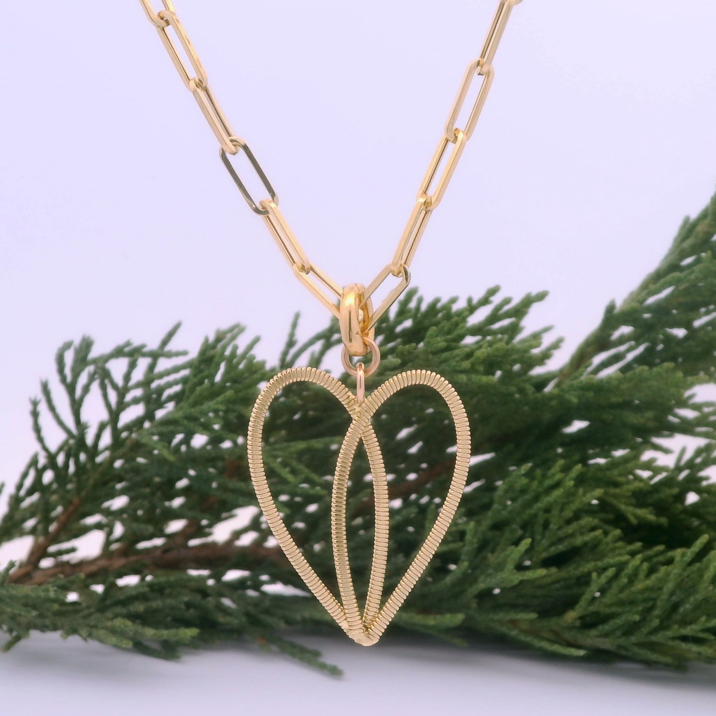 Gold guitar string heart on gold paperclip chain with white background and pine branch