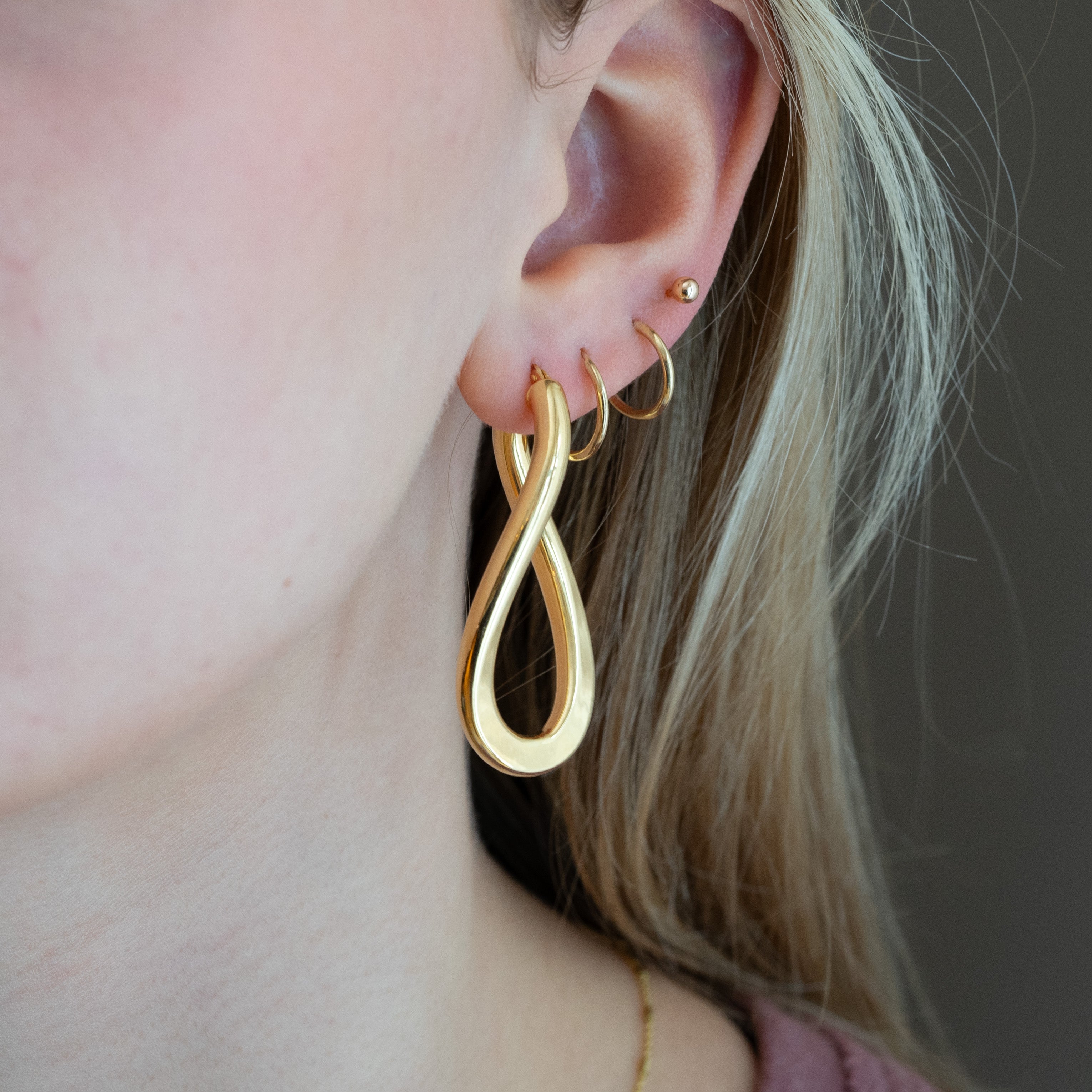Gold infinity hoop earrings worn by a person with a neutral background