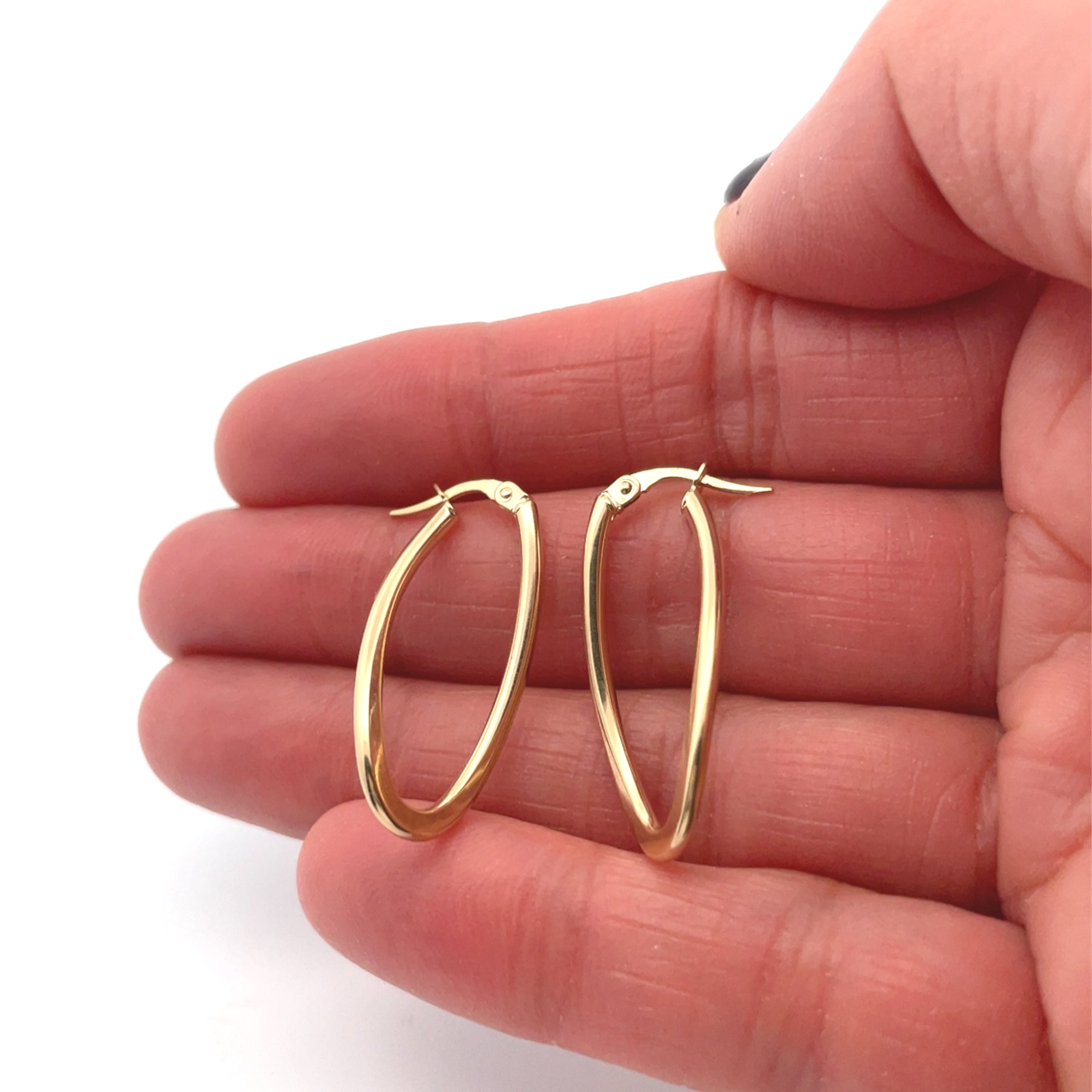 Gold hoop earrings held between fingers on a white background
