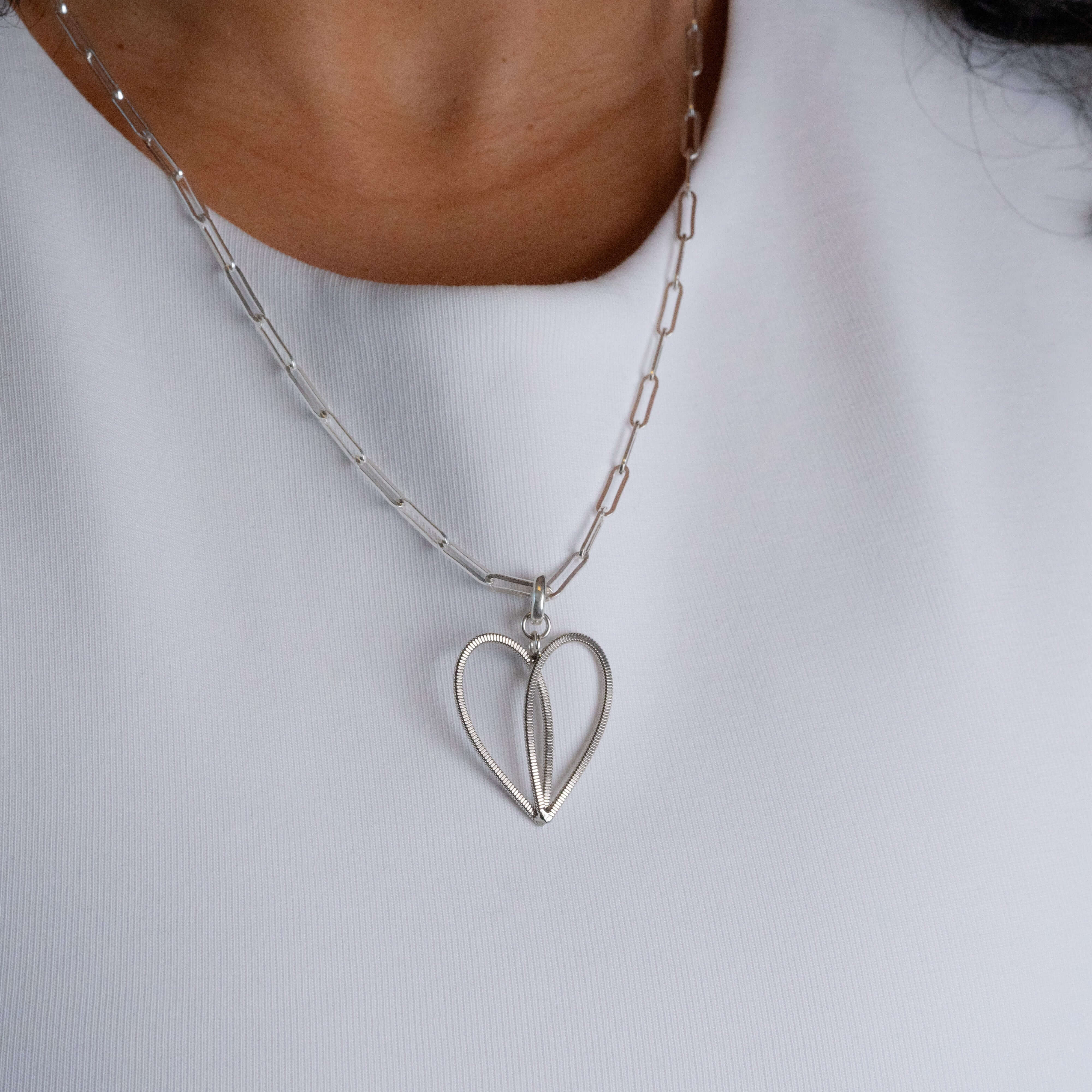 Rose gold guitar string heart with oval link silver chain on a model with white top.