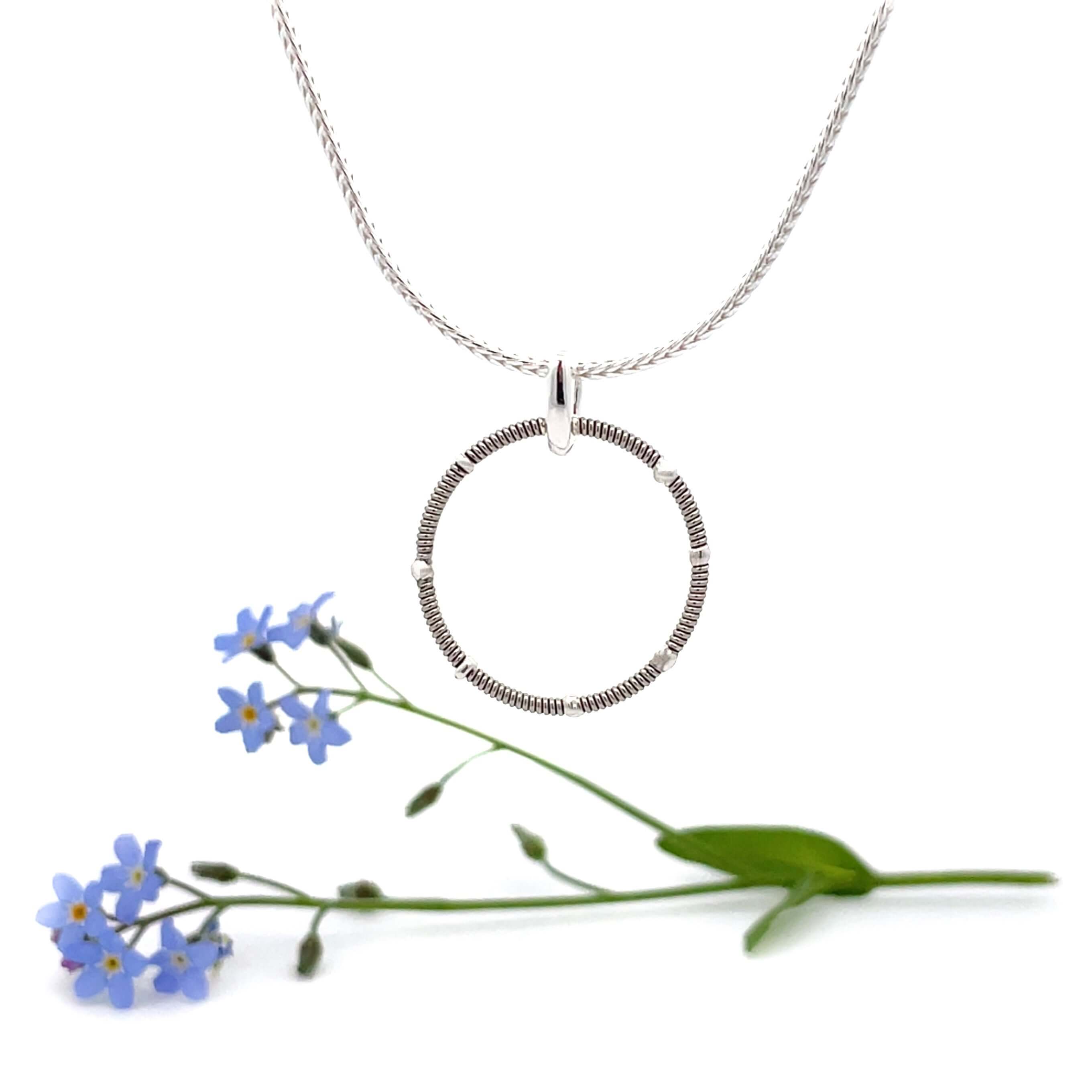 guitar string ring round pendant on silver chain with white background and blue flowers