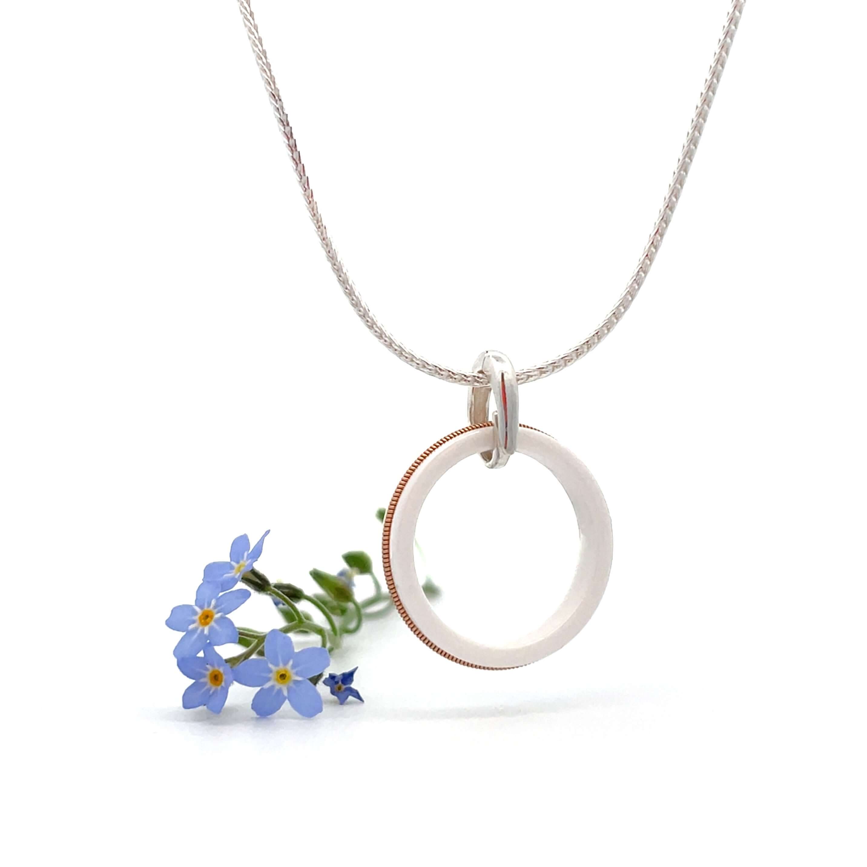 White guitar string ring round pendant on silver chain with white background and blue flowers