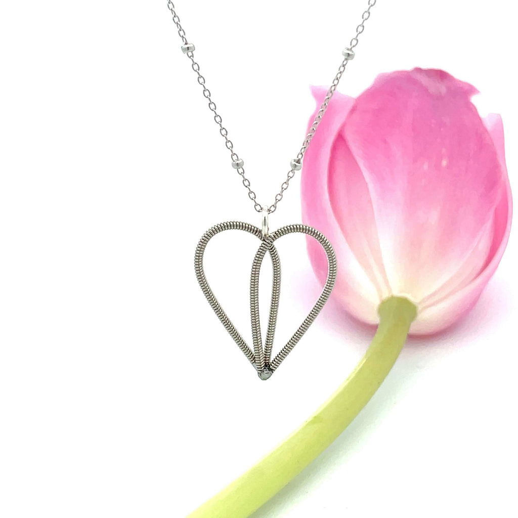 White gold guitar string heart necklace on white background with tulip.