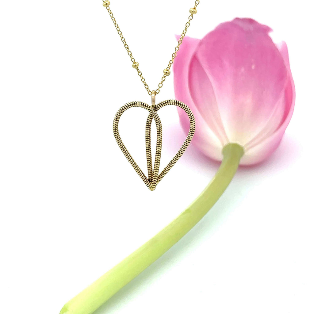 Gold guitar string heart necklace on a white background. with pink tulpi.