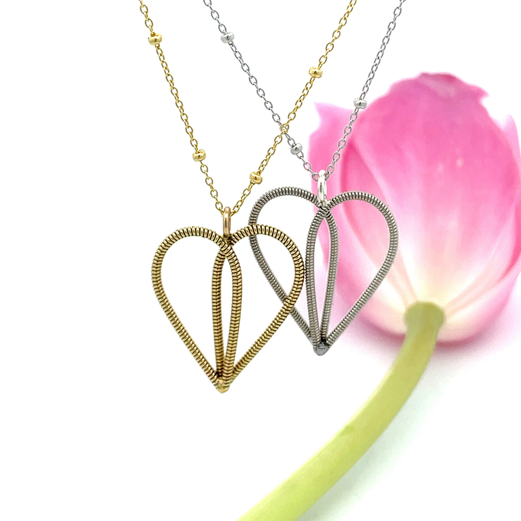guitar string heart necklaces on white background with pink tulip