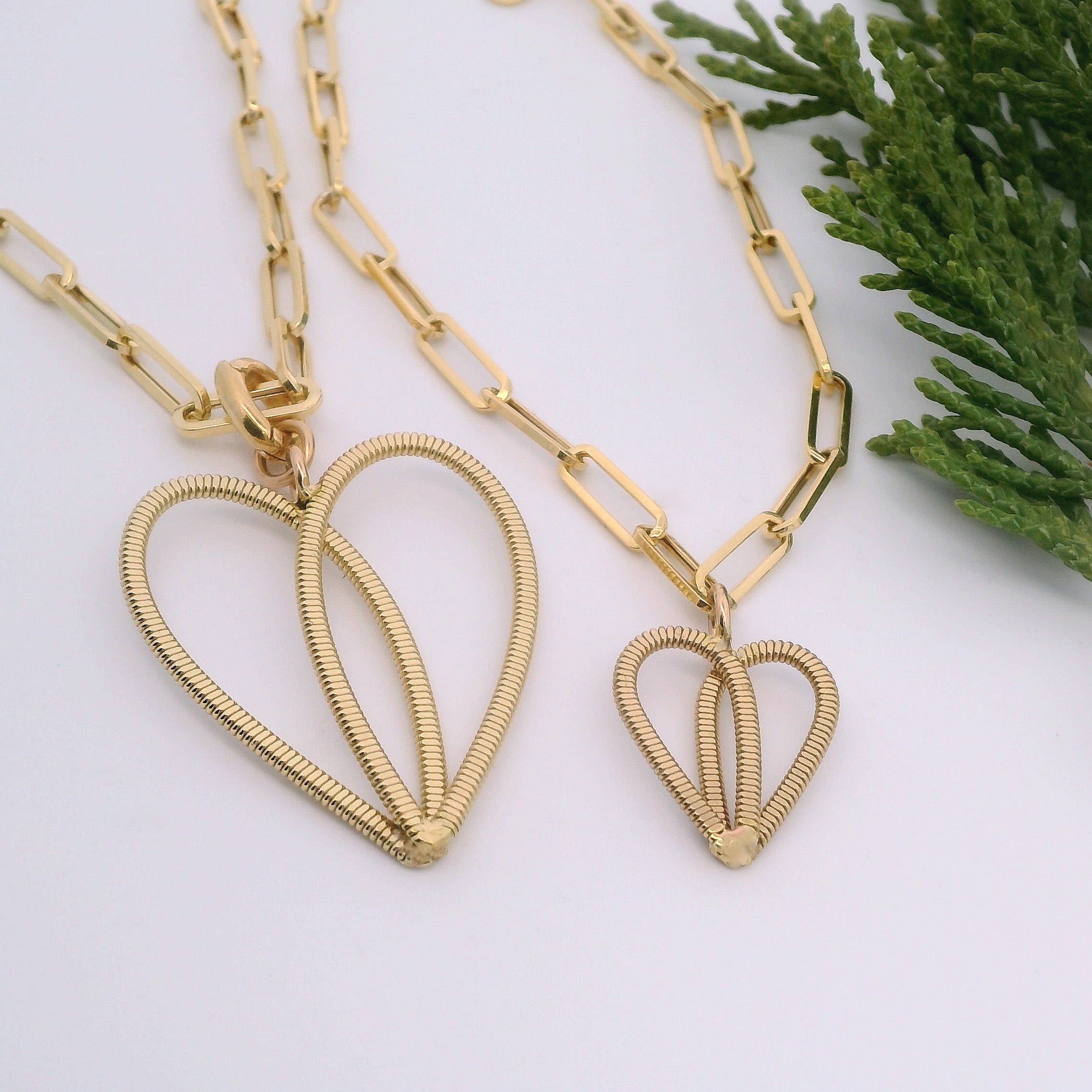 Gold guitar string heart on gold paperclip chain with white background and pine branch