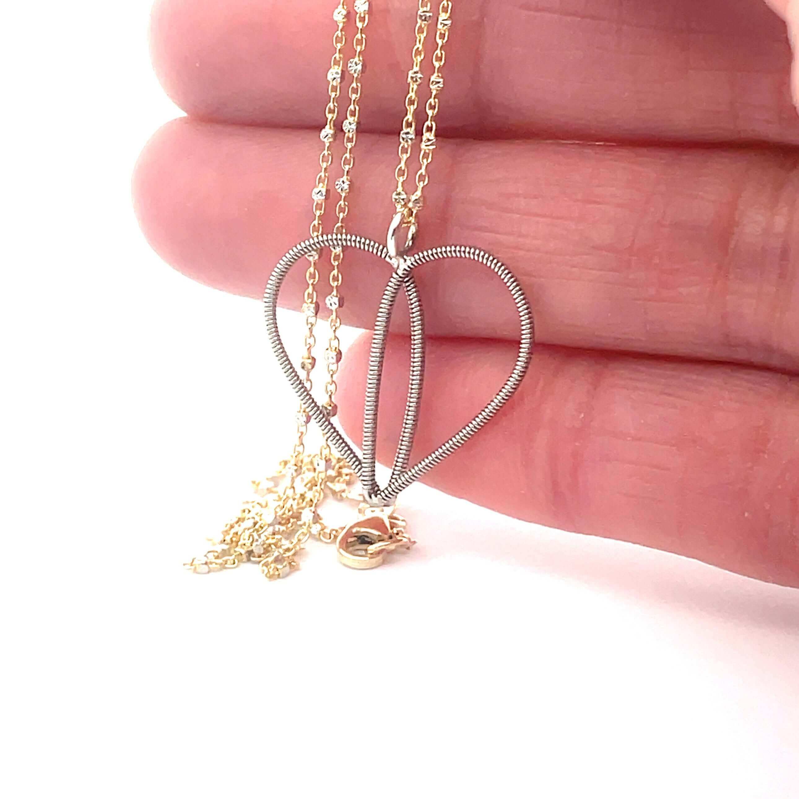 Silver guitar string heart necklace on  gold chain with white bead accents held  in hand.