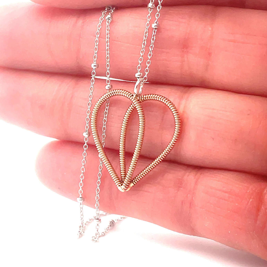 Guitar string heart on white gold chain against hand.