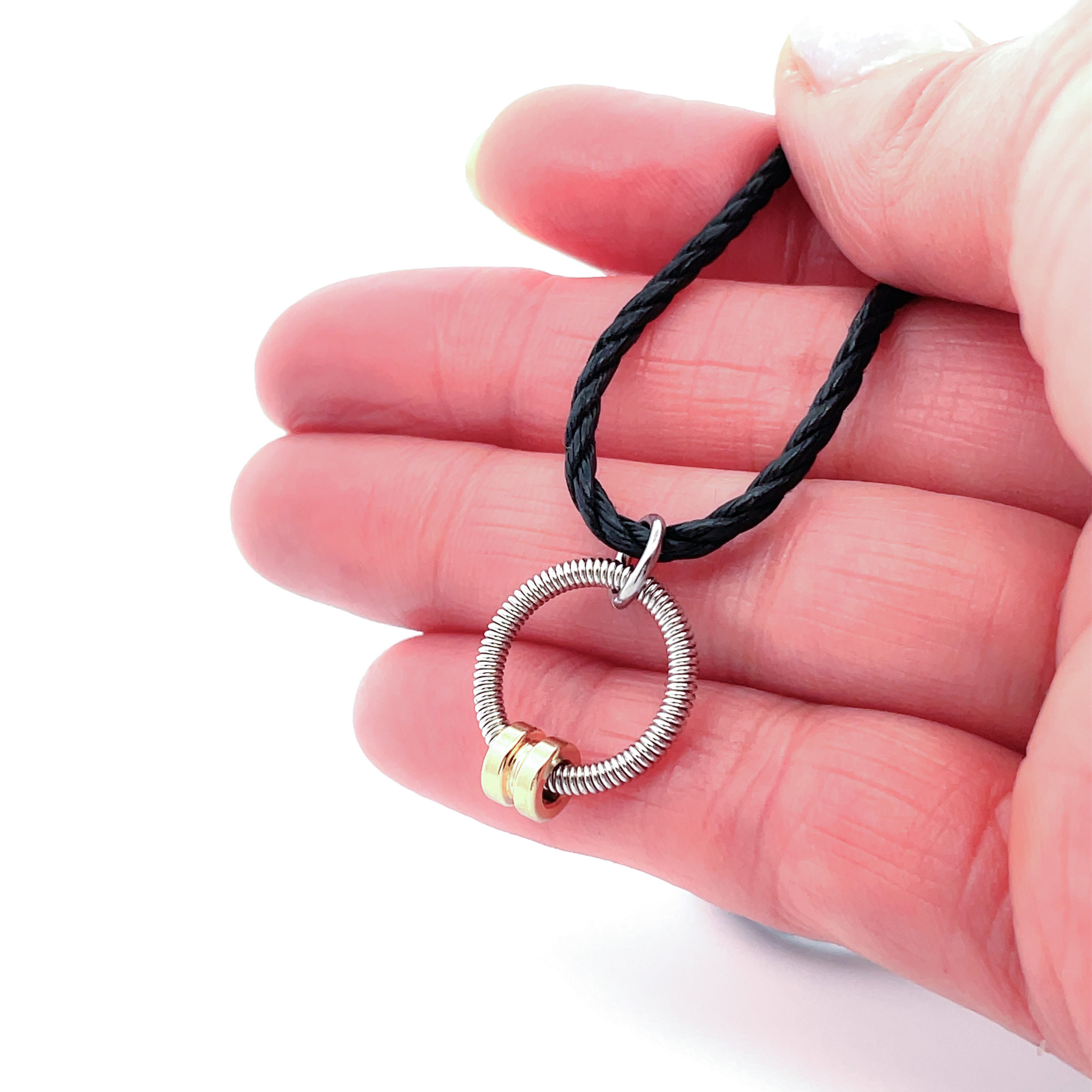 bass guitar string circle pendant with brass accent on black cord and  held in a hand.