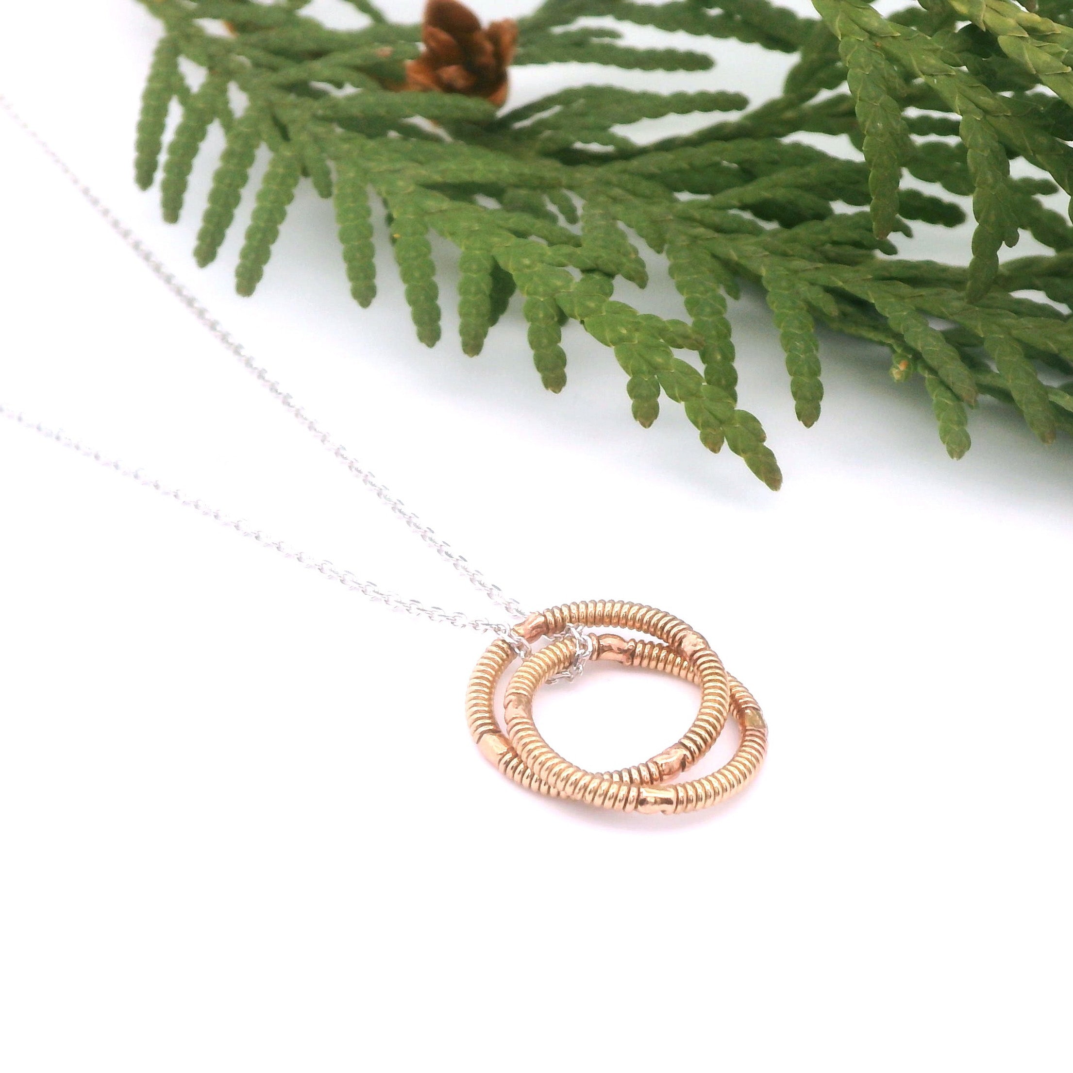 Necklace with a rose gold circular pendant on a white background with greenery.