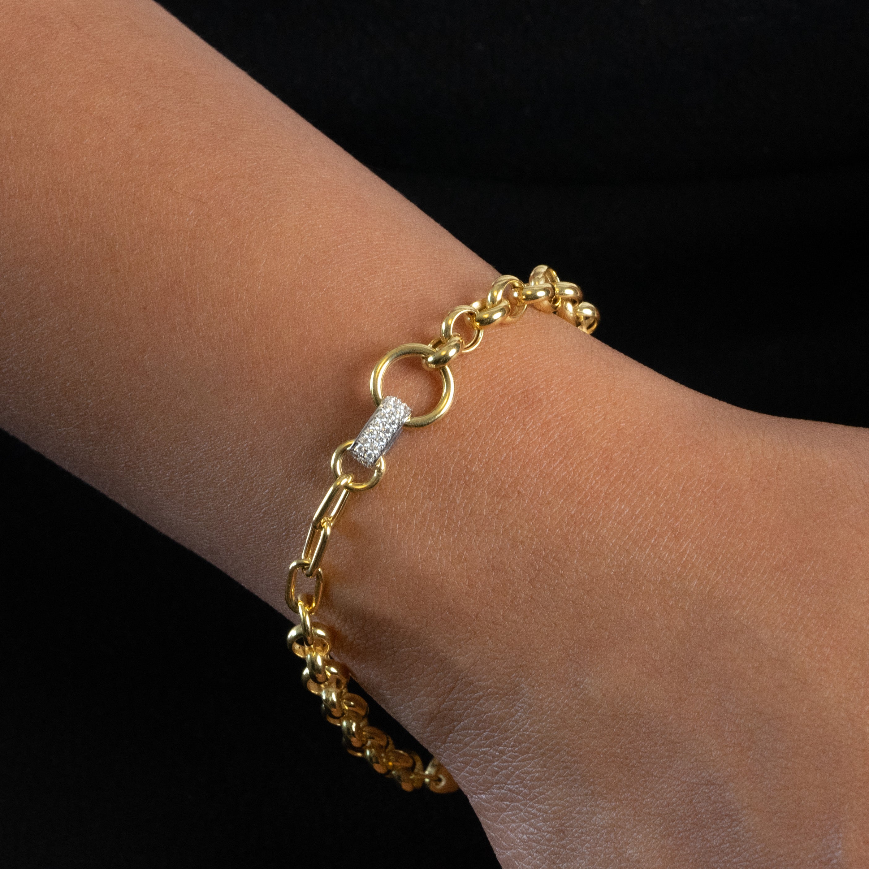 Gold bracelet with a diamond clasp on a wrist against a black background