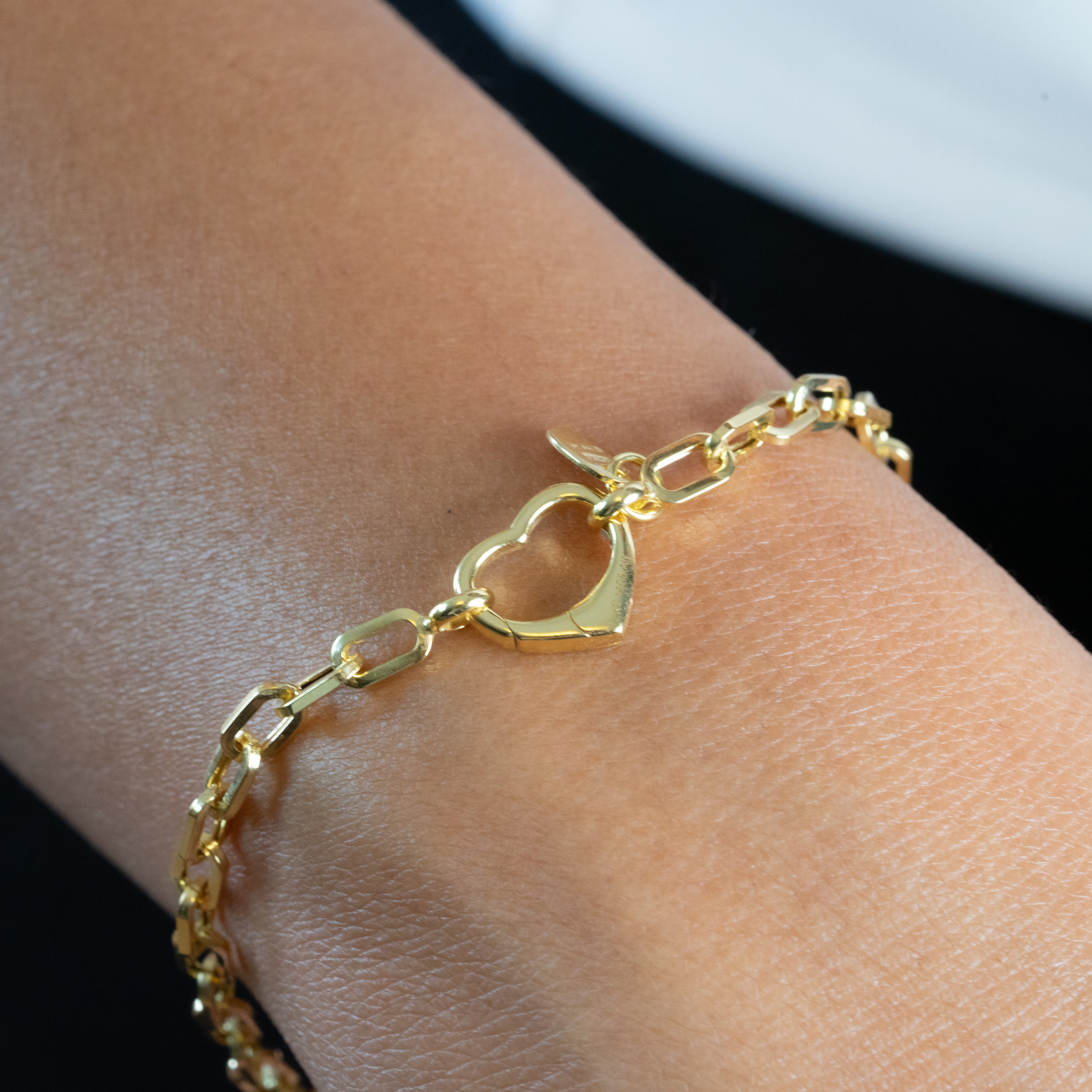 Gold bracelet with a heart clasp on a wrist against a neutral background