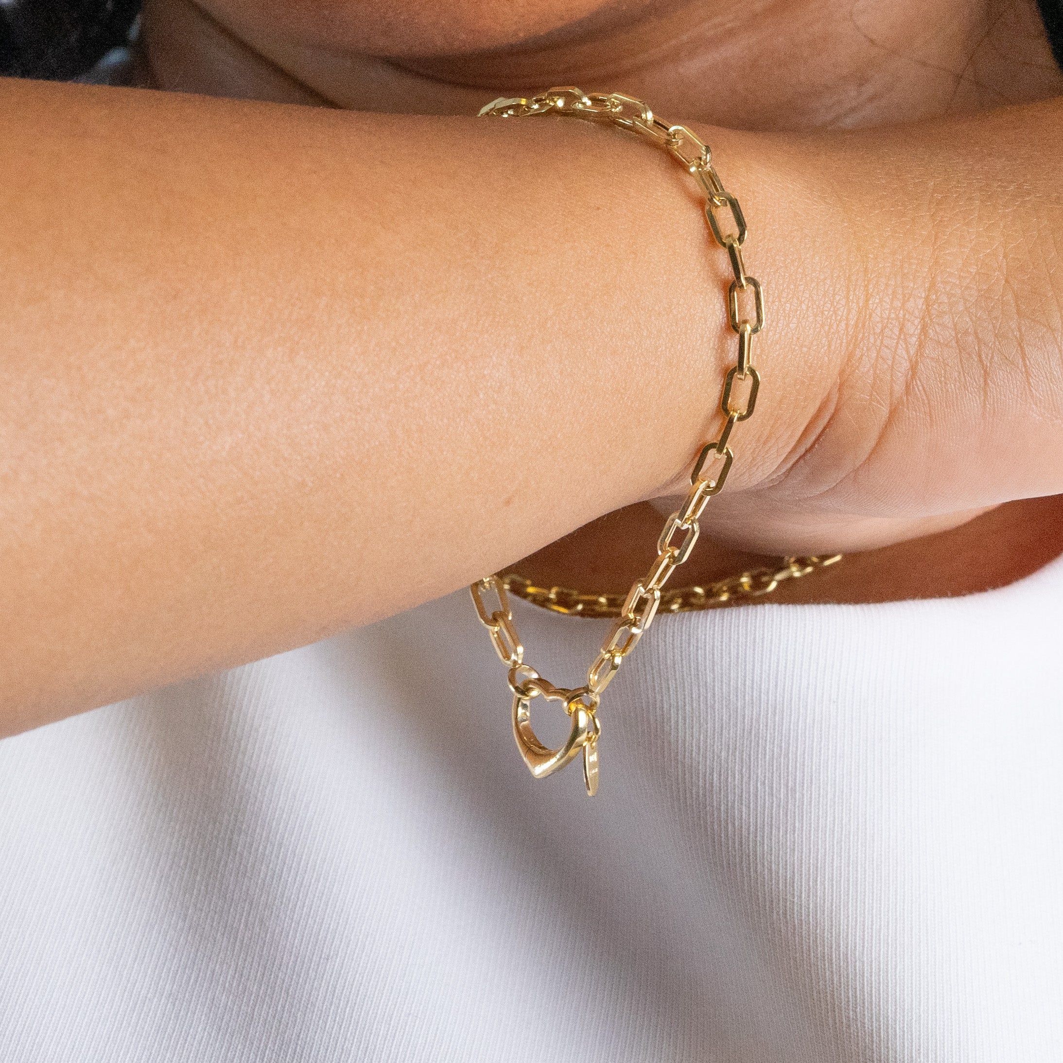 Gold paperclip link bracelet with heart charm hanging form wrist.