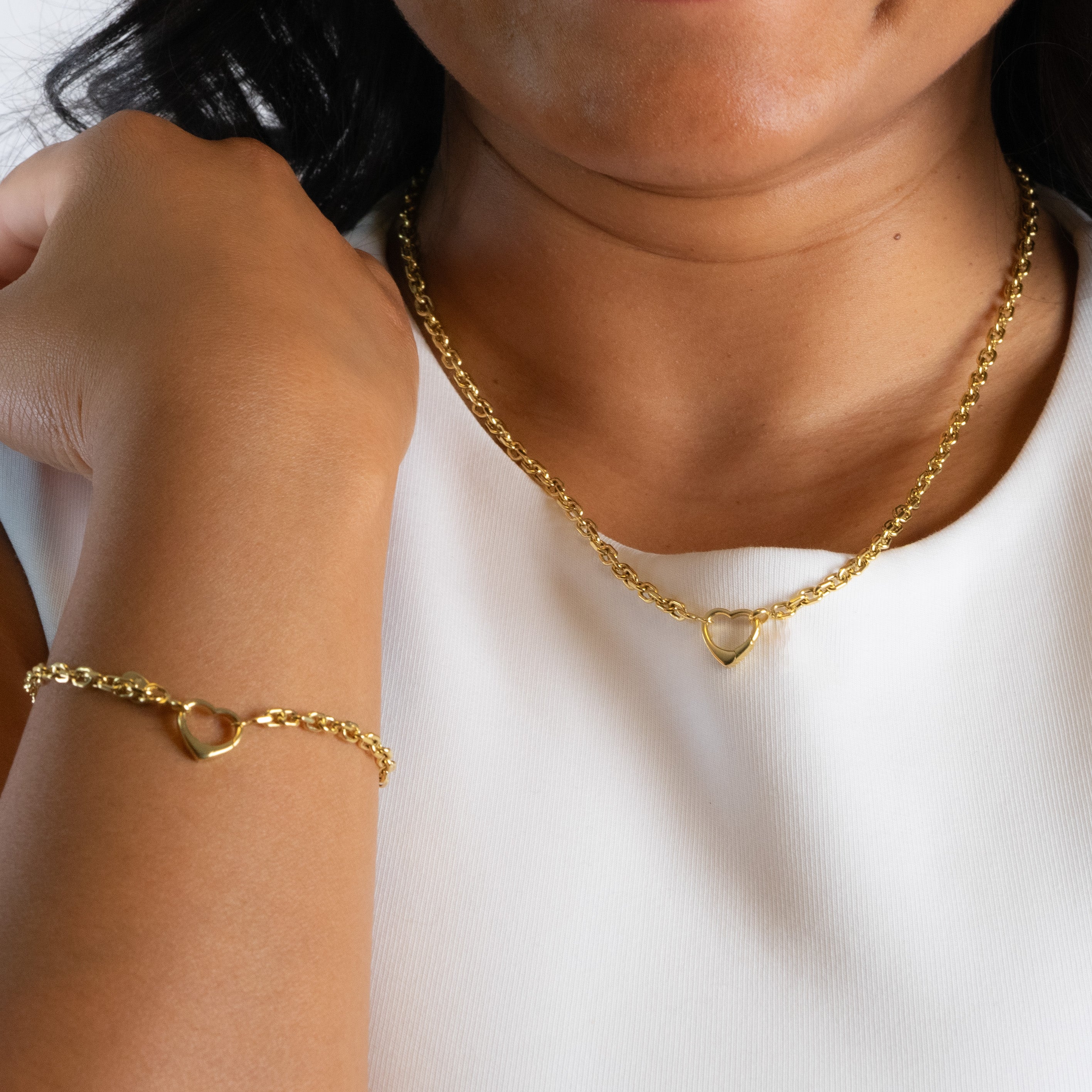 Gold chain necklace and bracelet with heart clasps on a person against a white background