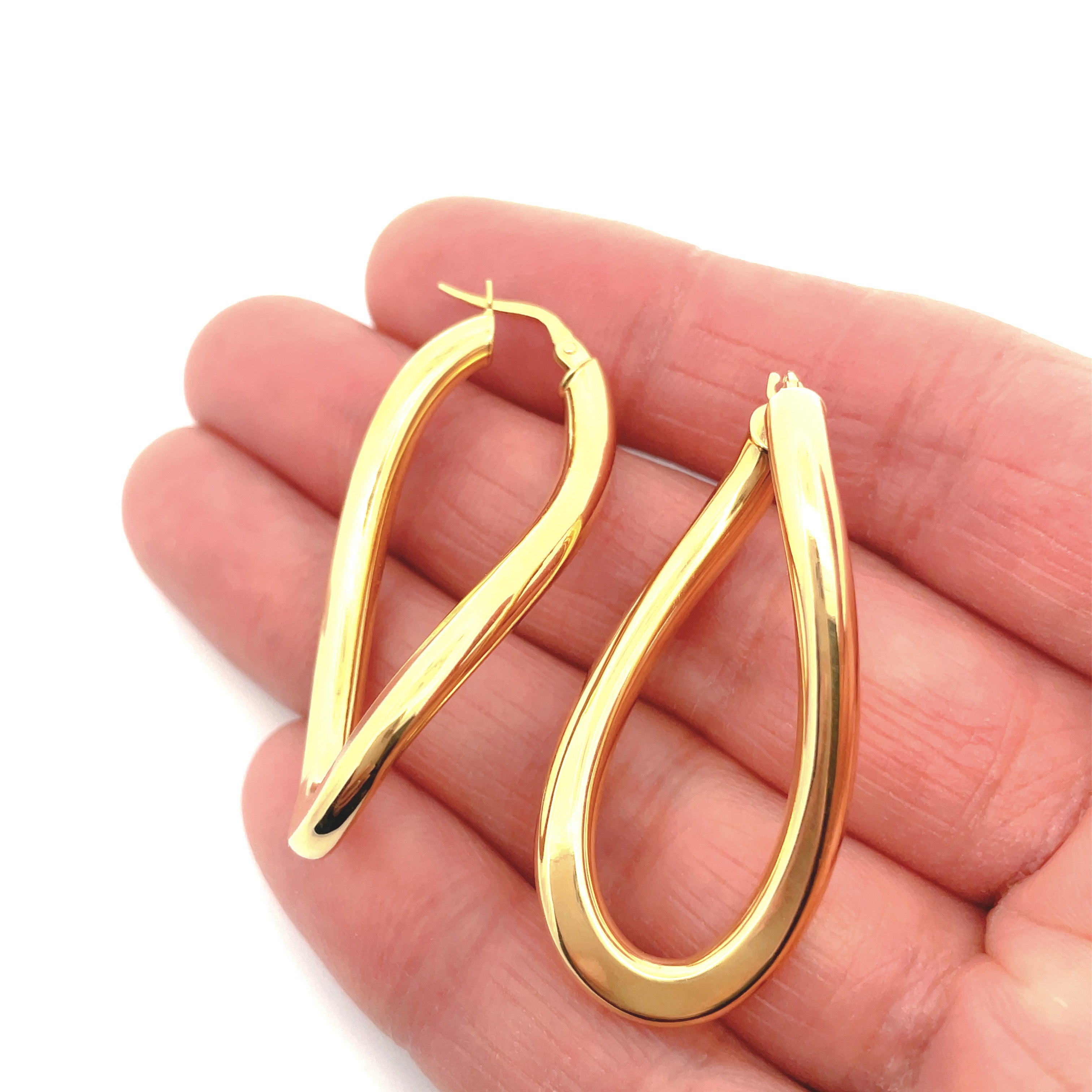 Gold hoop earrings held between fingers on a white background