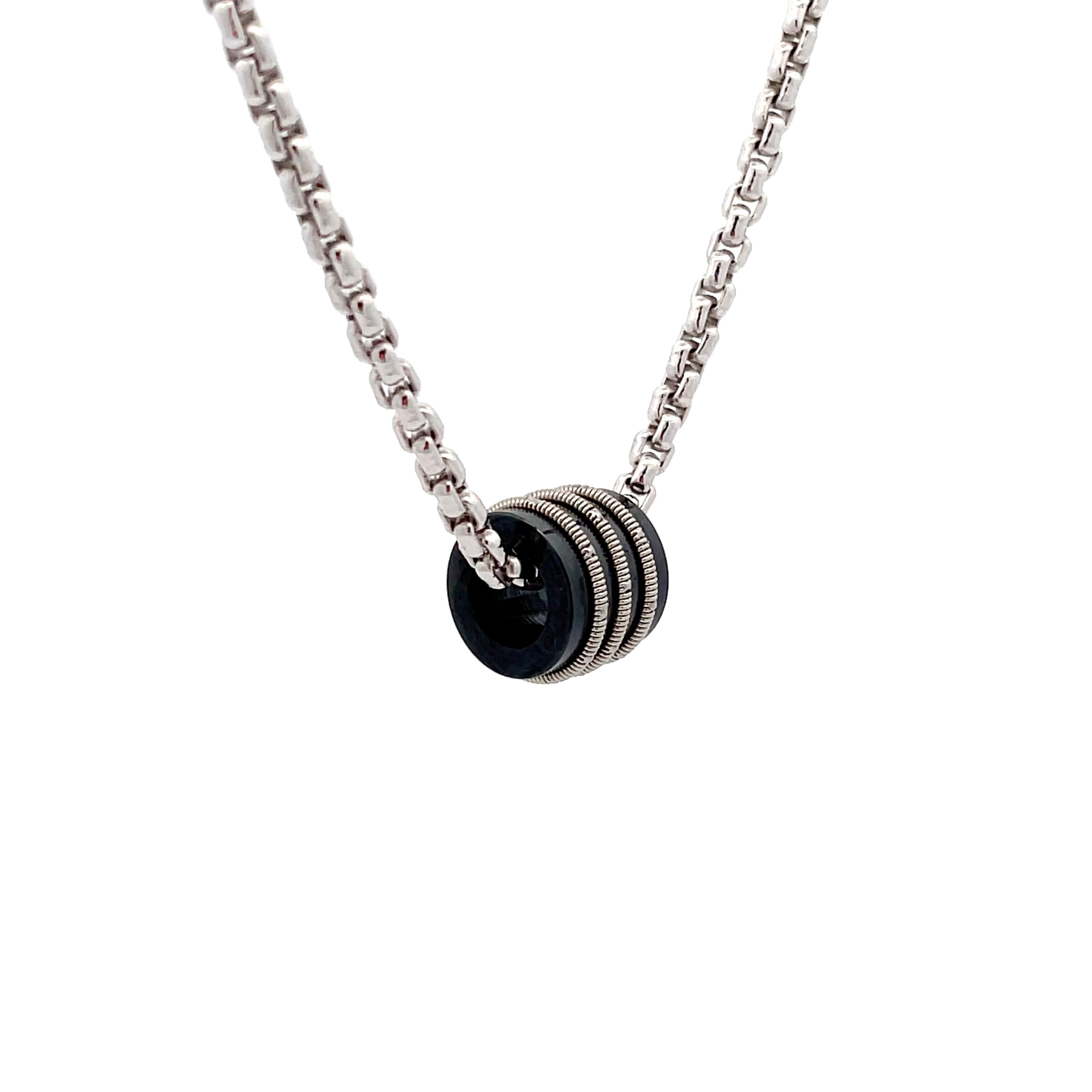 Silver necklace with black bead and inlaid guitar string on white background, side view.
