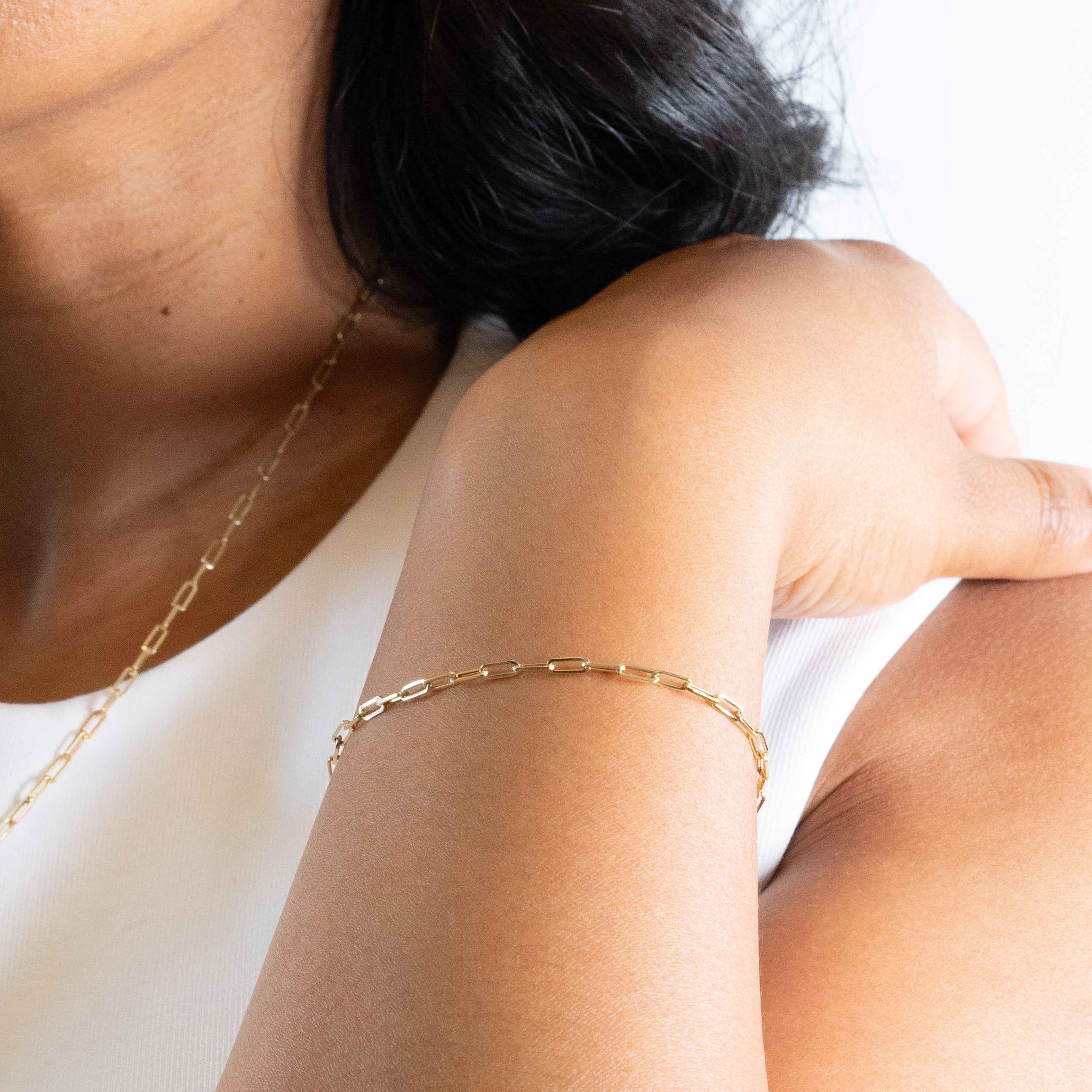 Gold paperclip bracelet on model with white shirt.