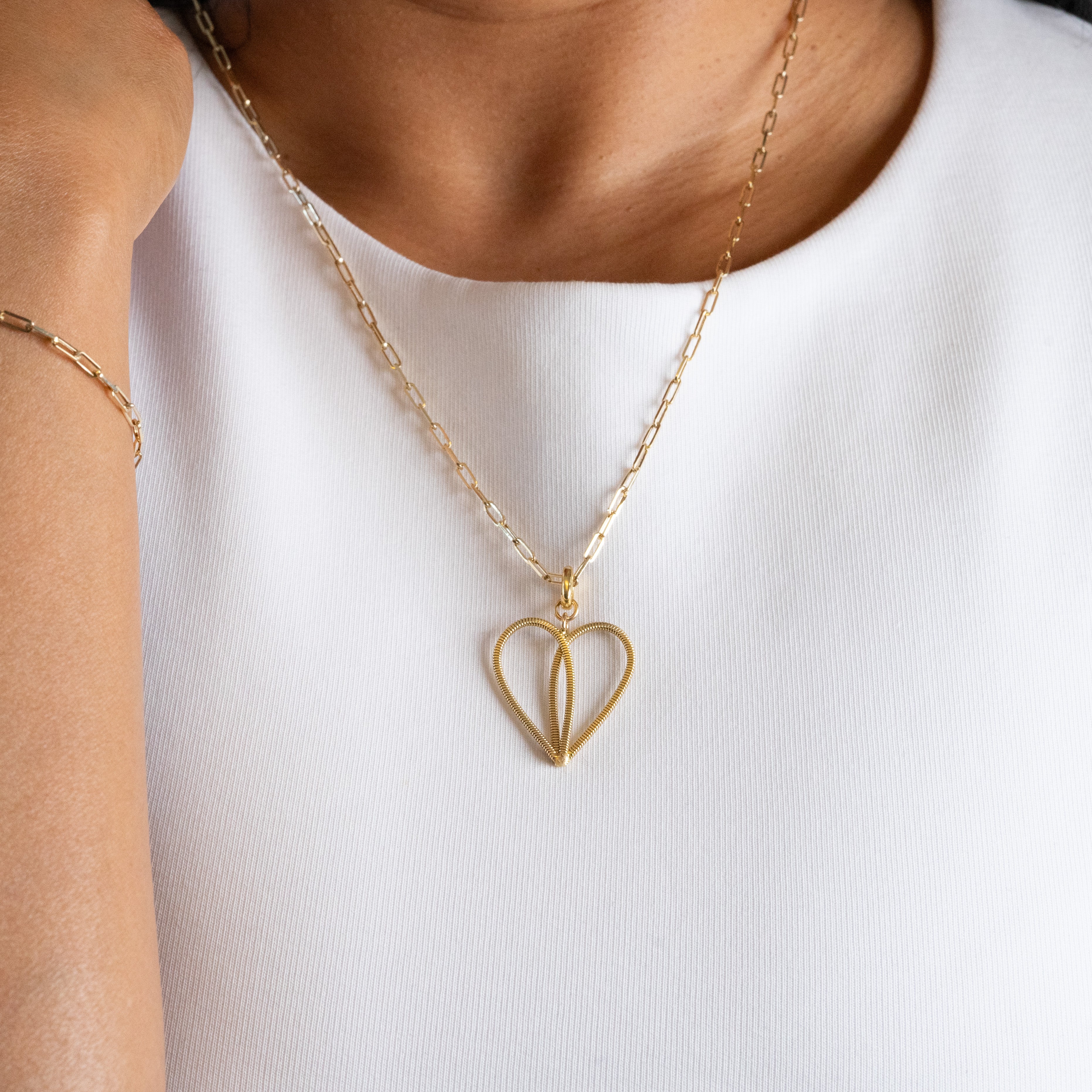 Gold guitar string heart-shaped necklace on a person wearing a white shirt