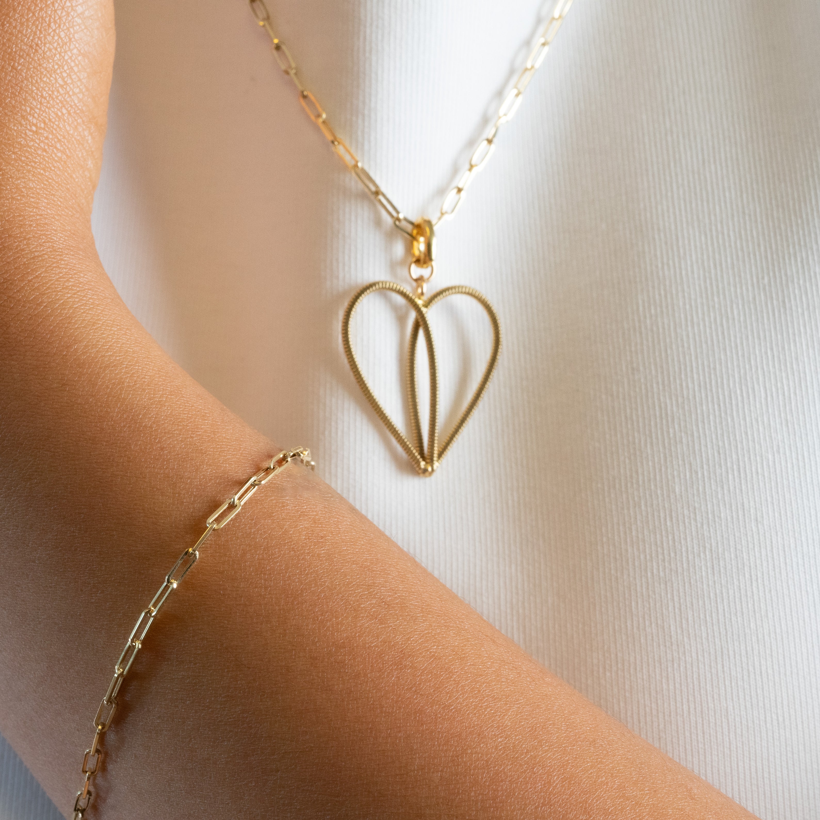 Gold guitar string heart-shaped necklace and gold bracelet on a person wearing a white shirt