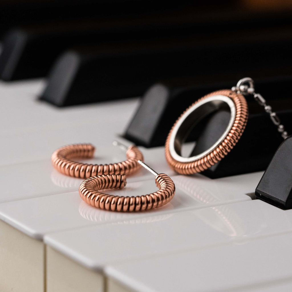 Piano string ring necklace and hoop earrings resting against piano keys