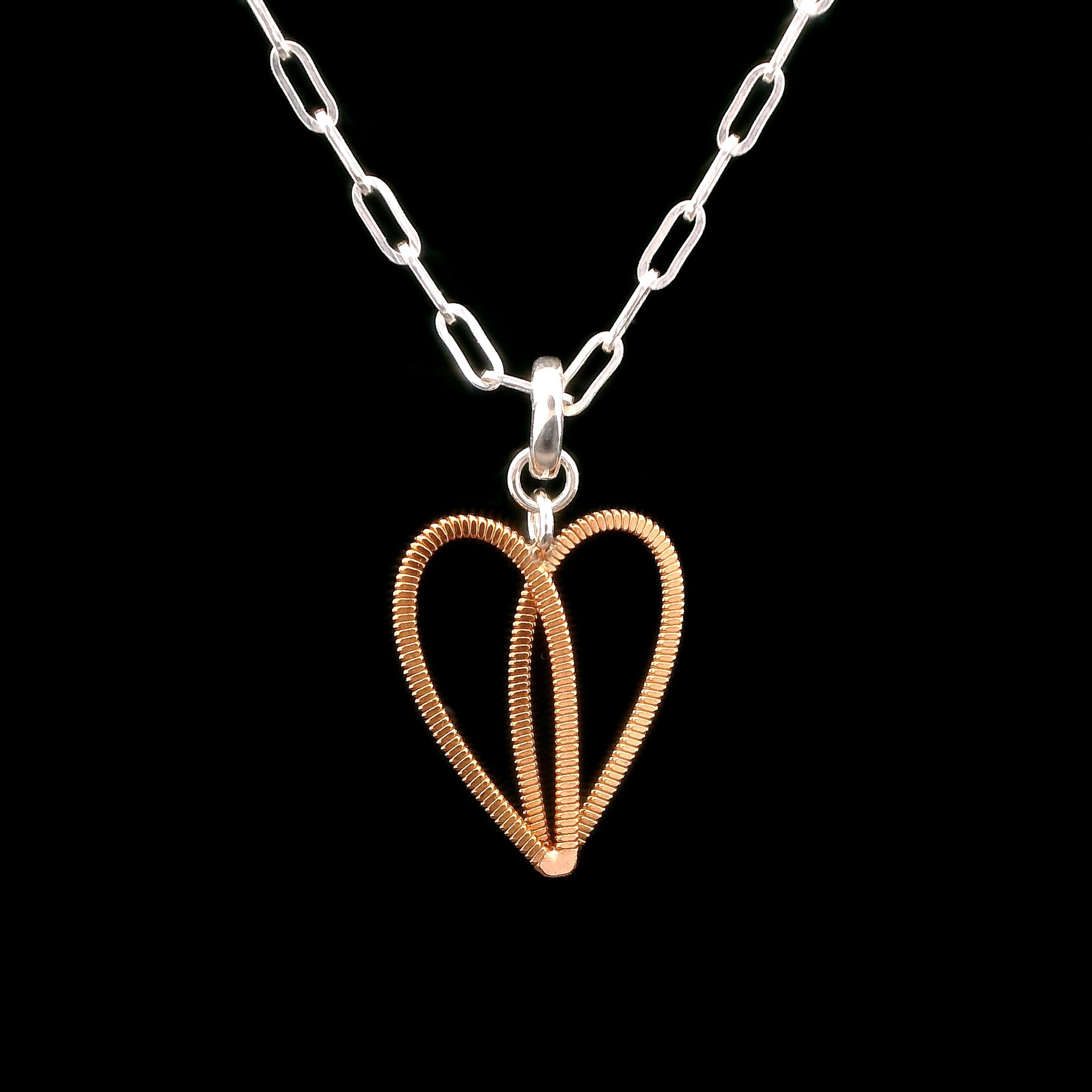 Guitar string heart pendant on silver paperclip chain with black background.
