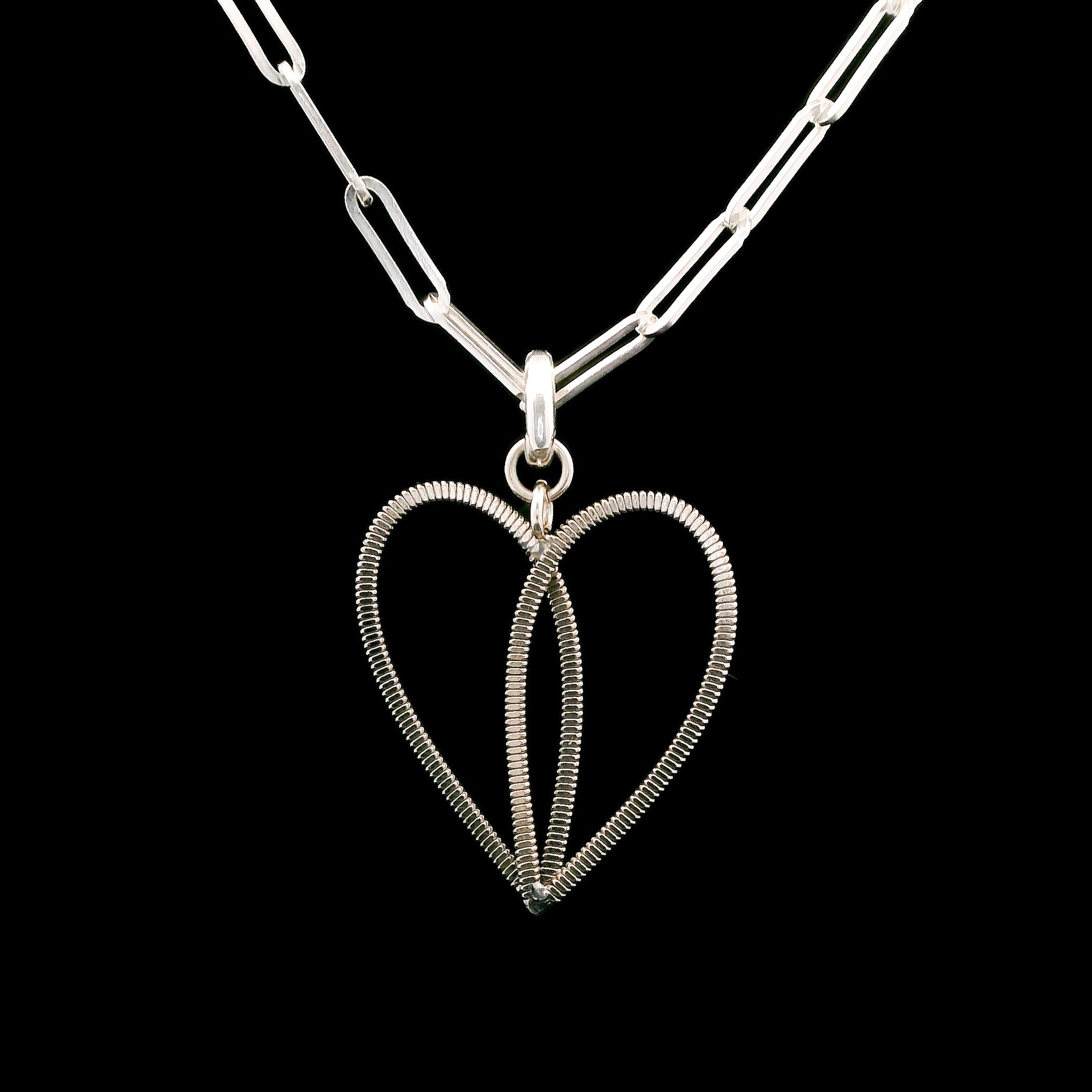 Silver heart-shaped guittar string pendant on a paperclip chain against a black background